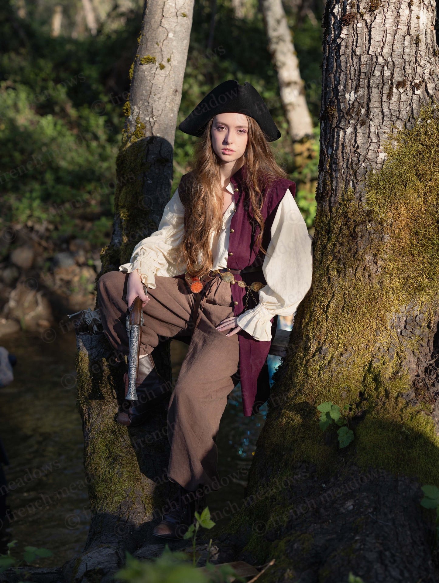Young woman wearing a Burgundy Pirate Vest in deep burgundy, styled with historical costume outdoors by trees.