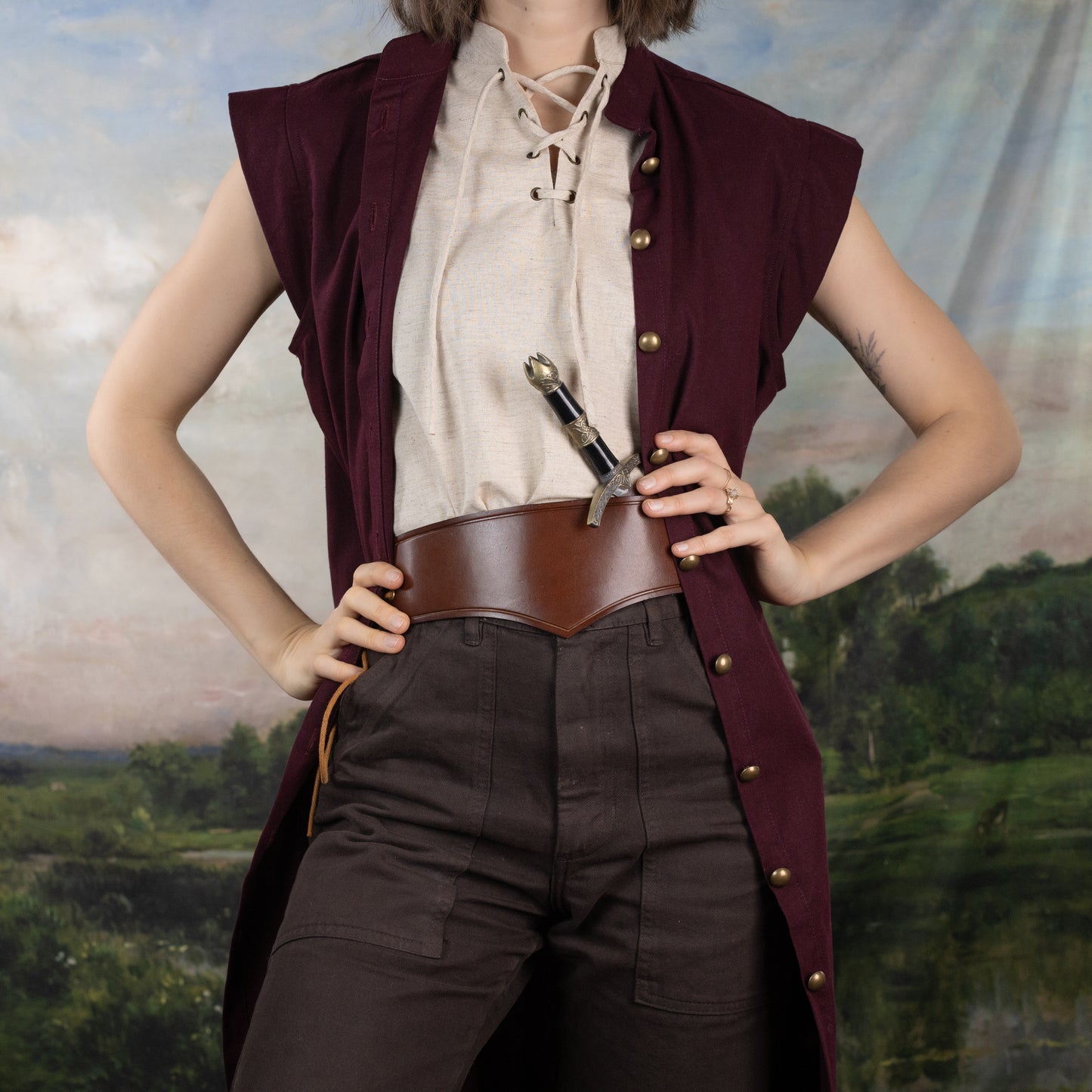 Woman wearing a Burgundy Pirate Vest over a laced shirt and wide leather belt with dark pants in a rustic backdrop.