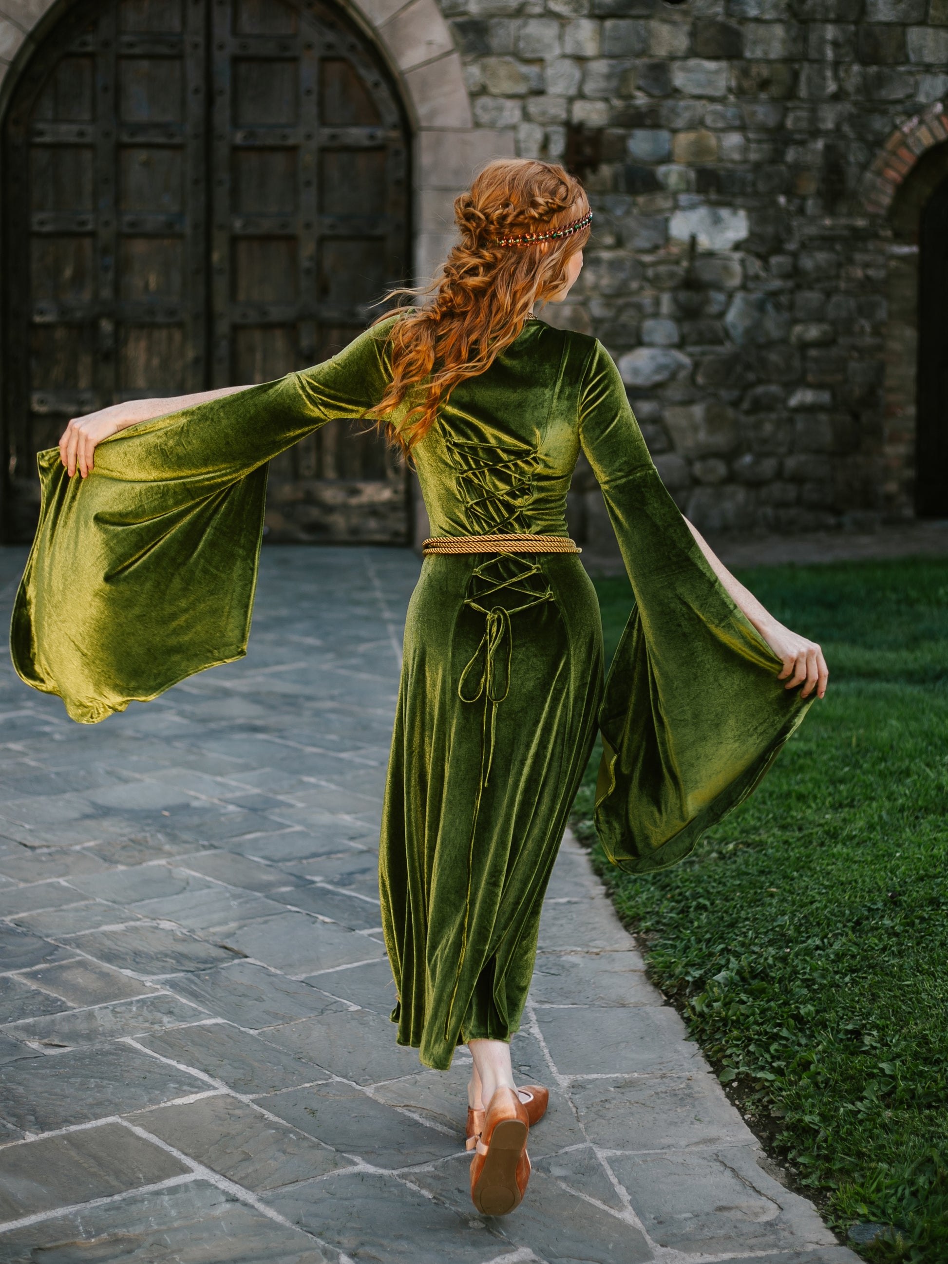 Medieval-inspired green velvet gown with flowing sleeves worn by woman with red hair and golden rope belt at waist