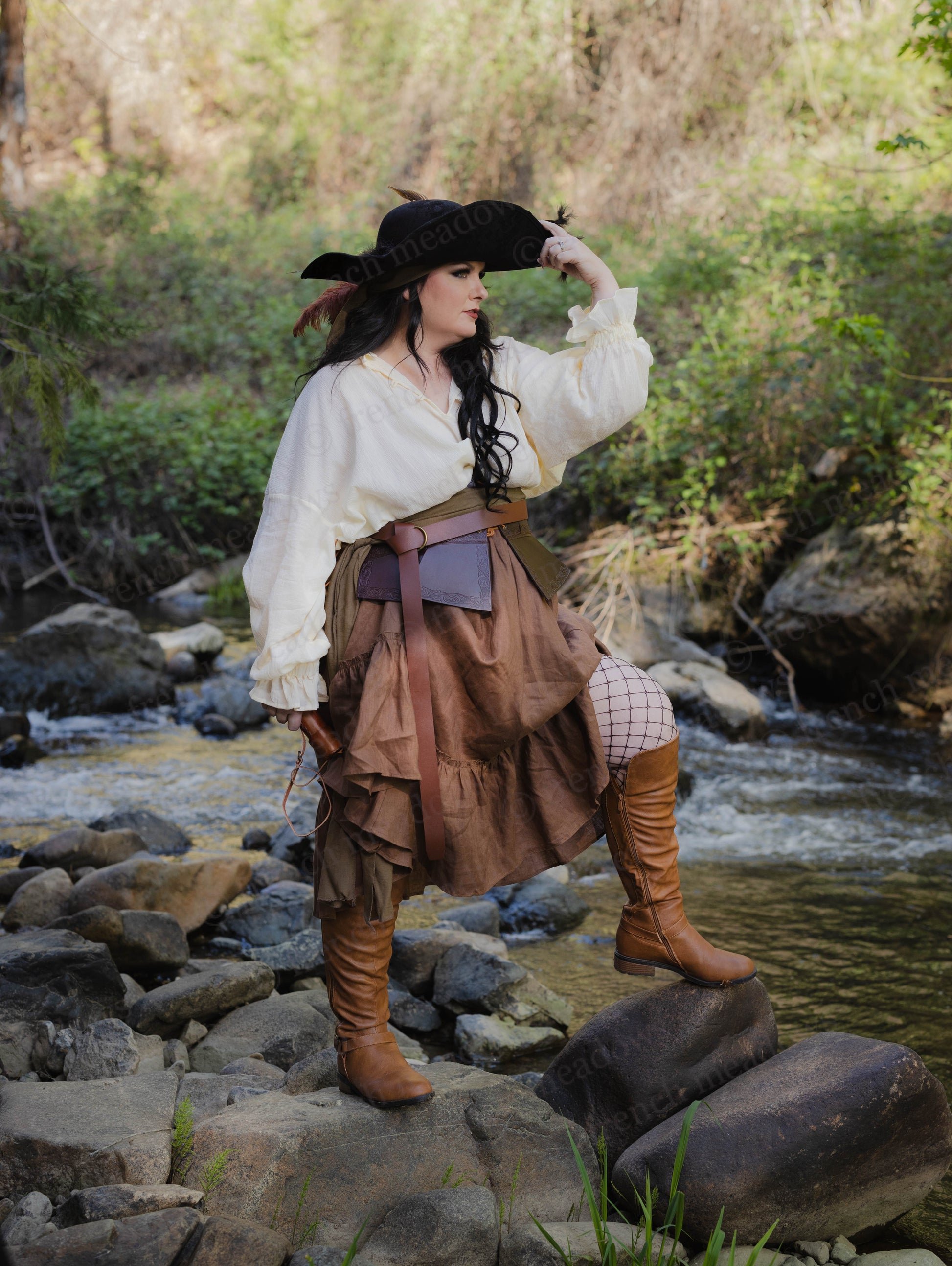Brown linen ruffle skirt shown in rustic outdoor setting with renaissance-inspired styling and tricorn hat by stream