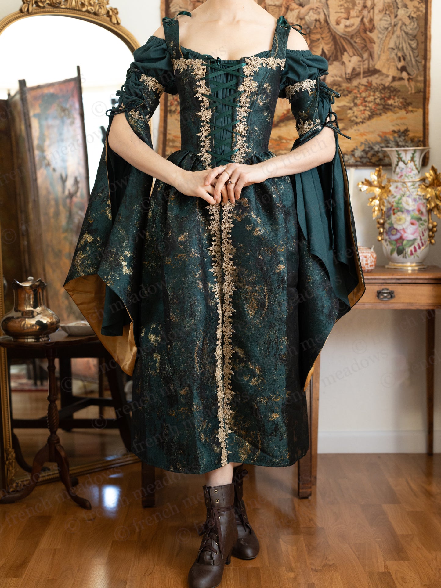 Dark green jacquard corset dress with gold trim and bell sleeves displayed on form in medieval-inspired setting