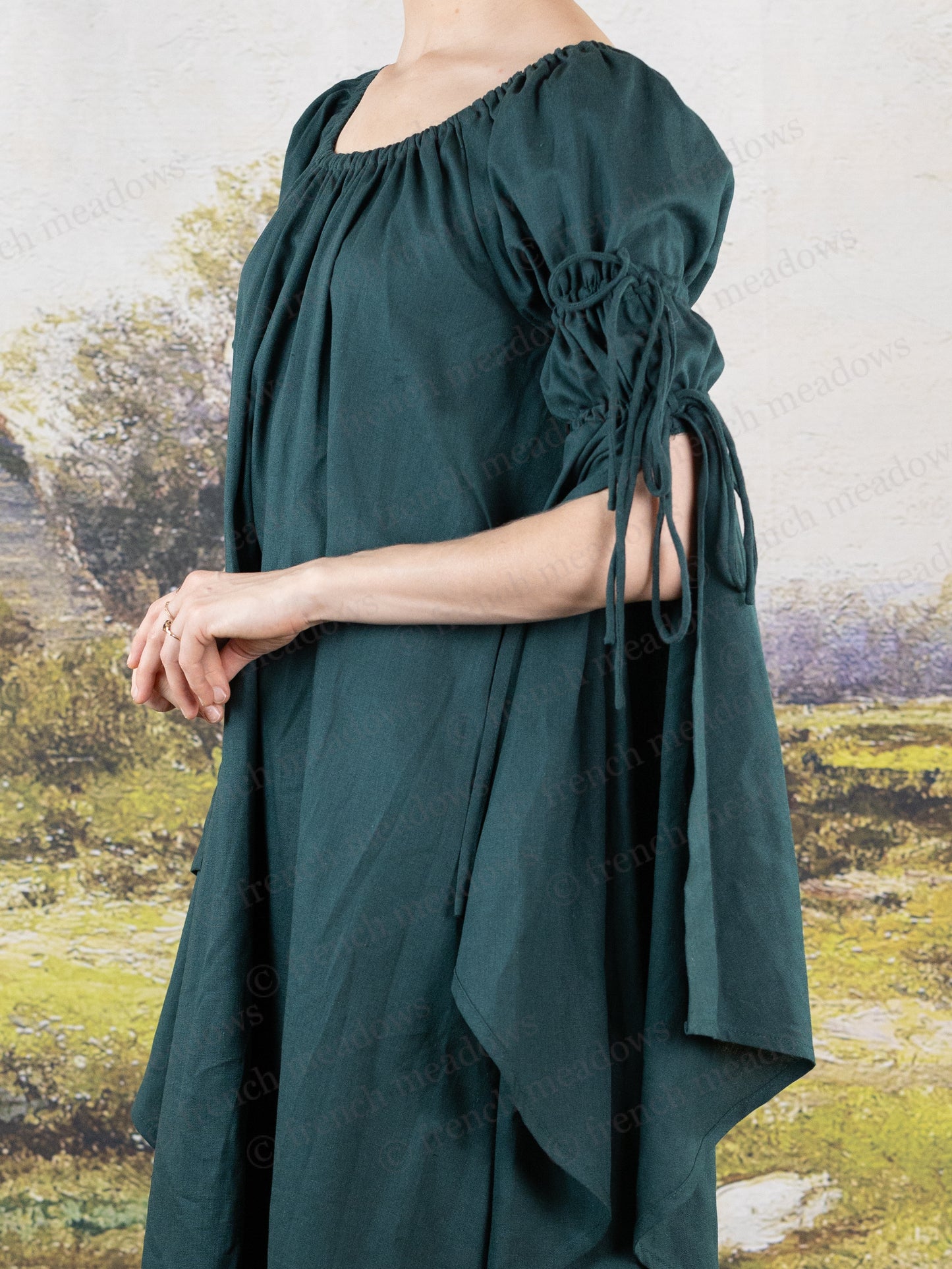 Dark green linen bell sleeve chemise with gathered neckline and flowing medieval-style sleeves shown against pastoral background
