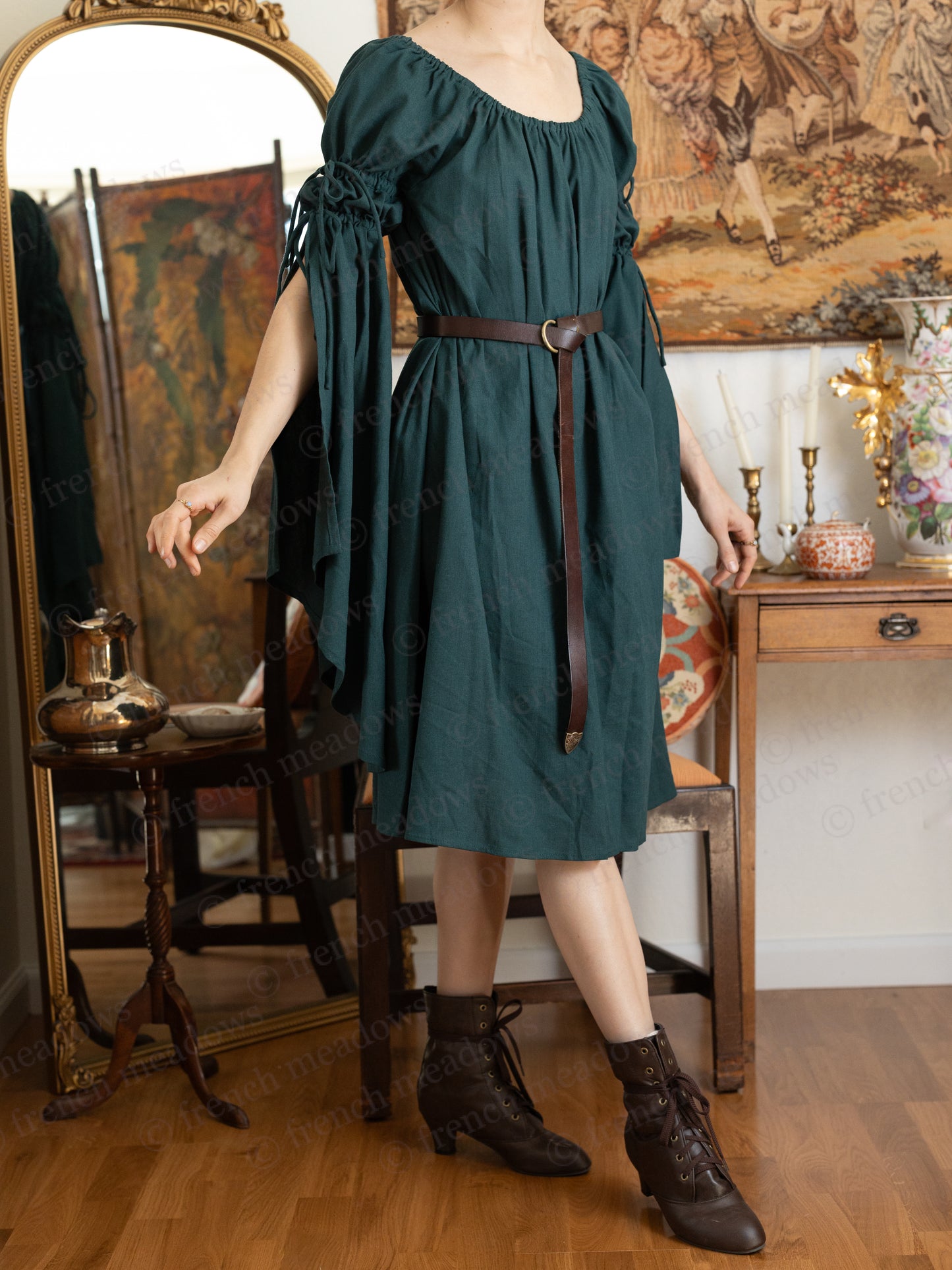 Dark green linen bell sleeve chemise dress with brown belt, shown in medieval-inspired setting with vintage mirror and decor