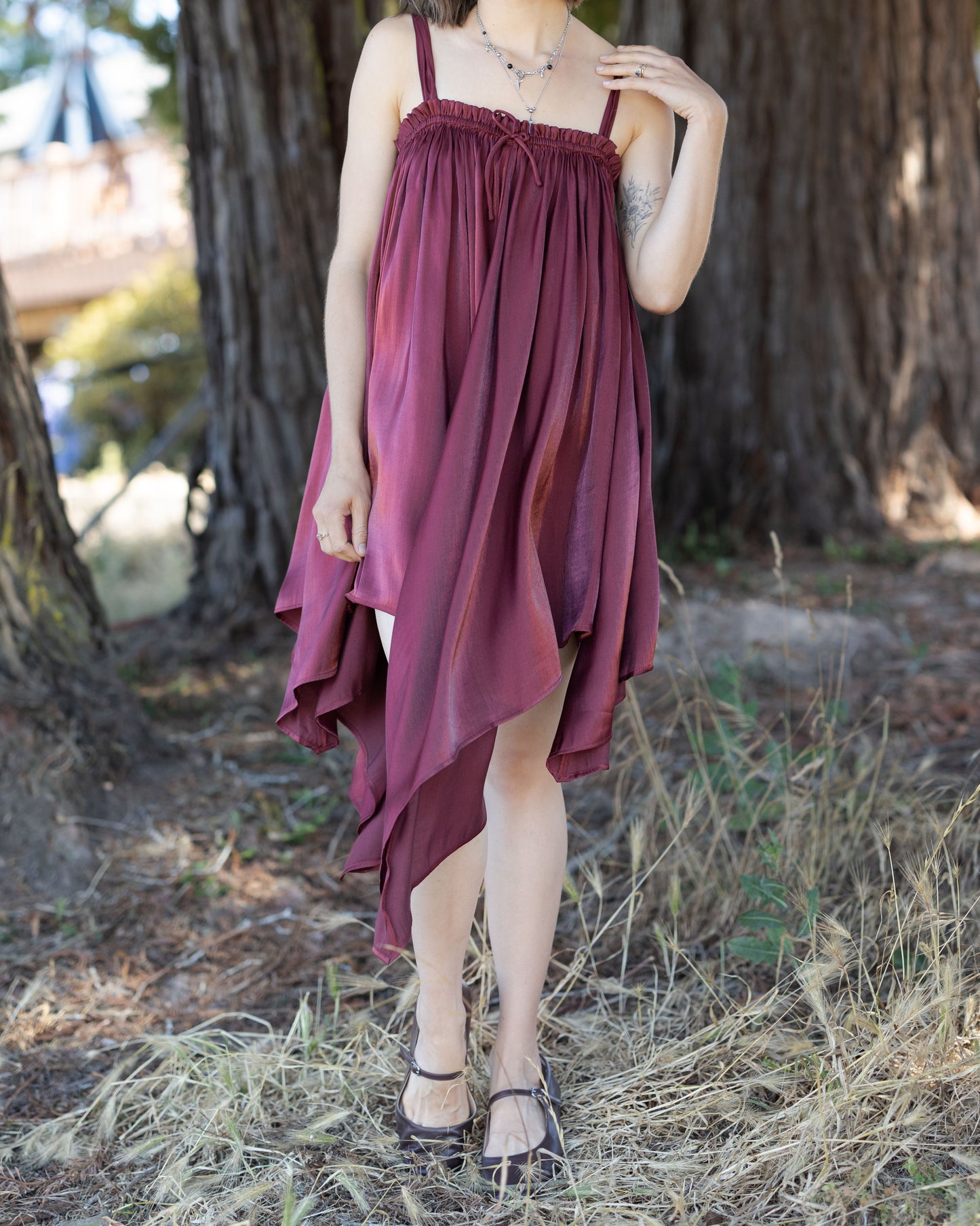 Woman wearing a Dark Red Flutter Dress with a flowing handkerchief hem standing outdoors near a large tree trunk