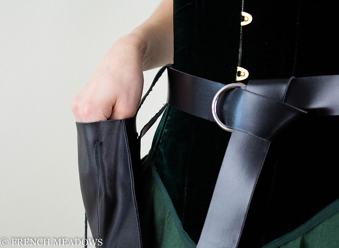 Drawstring pouch in black vegan leather shown attached to medieval-style belt with silver buckle against green and black costume
