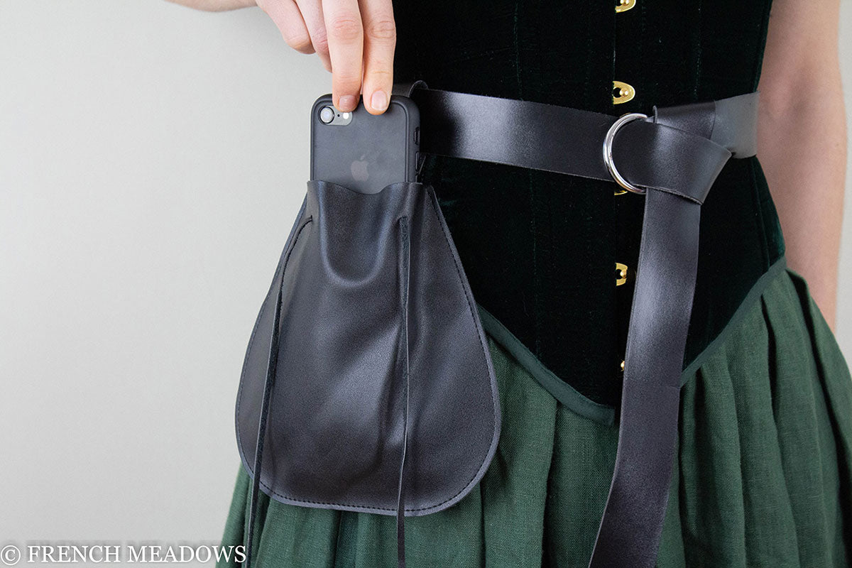 Black vegan leather drawstring pouch attached to belt against green skirt and black bodice, medieval costume accessory