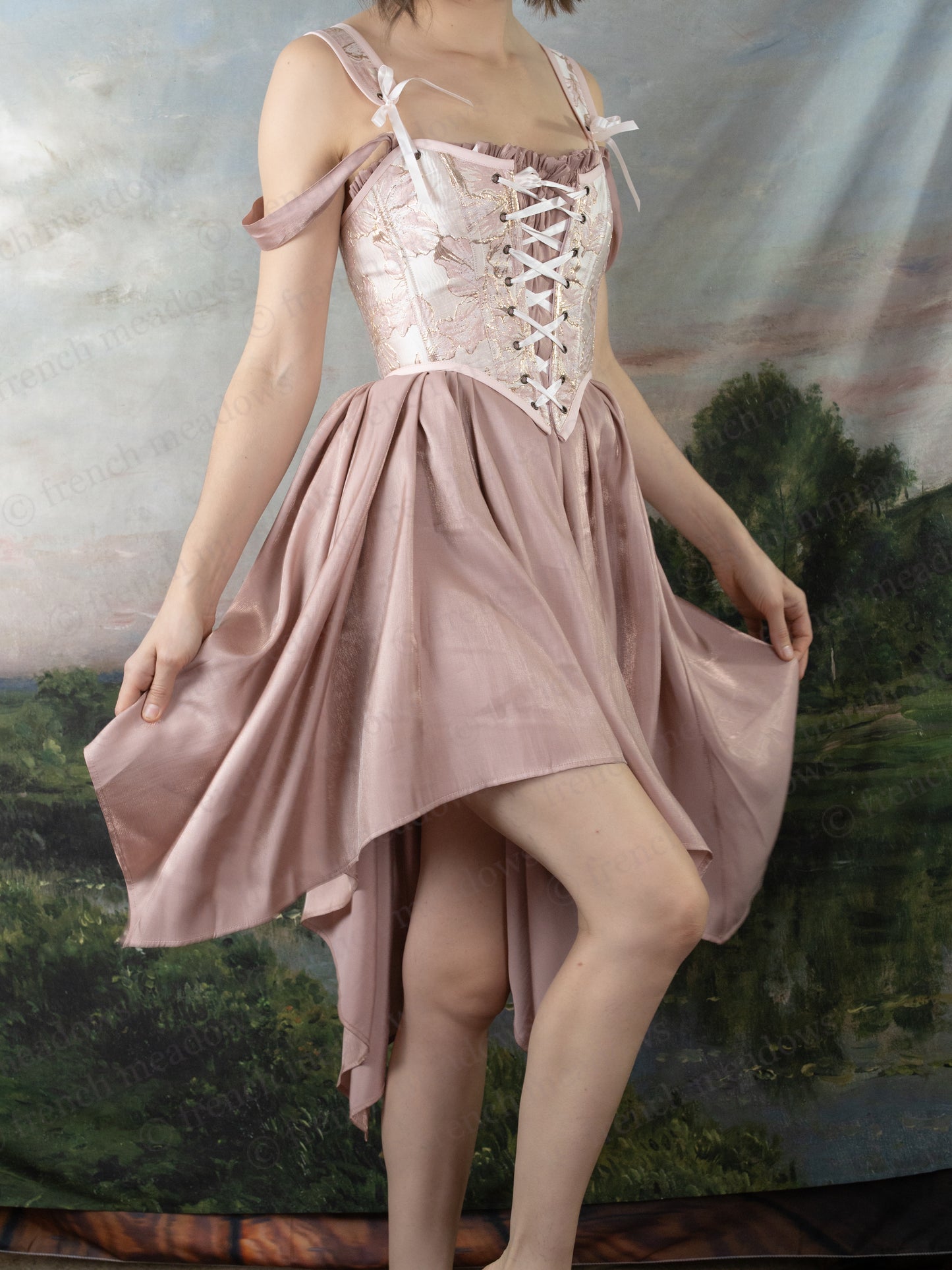 Woman wearing a pink handkerchief hem Flutter Fairy Dress with adjustable straps and corset-style bodice.