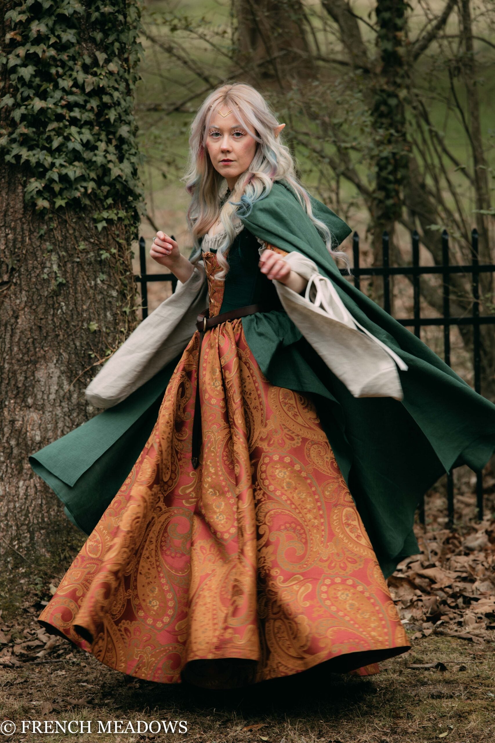 Linen Renaissance Cloak flowing in forest setting, layered over ornate orange dress with green outer layer and cream lining