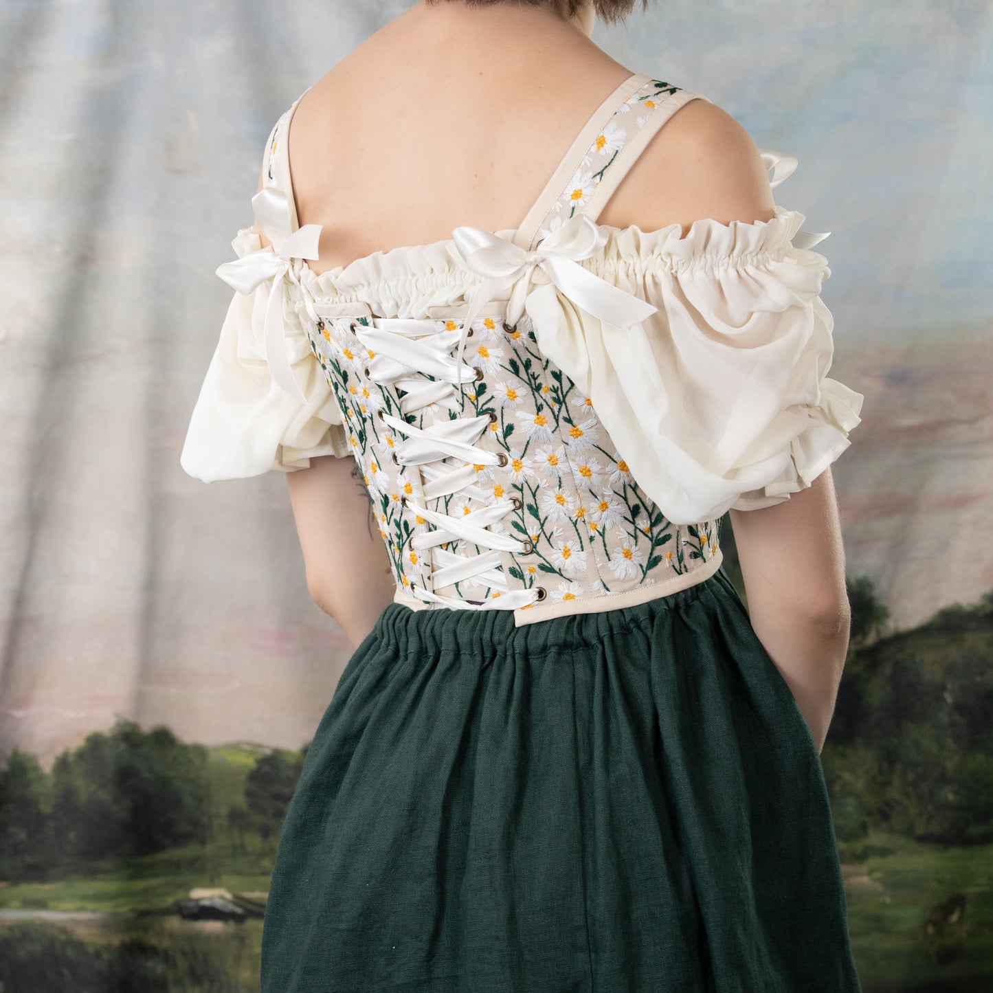 Embroidered Daisies Corset Top shown from back, featuring white puffy sleeves, floral embroidery, and lace-up detail with green skirt