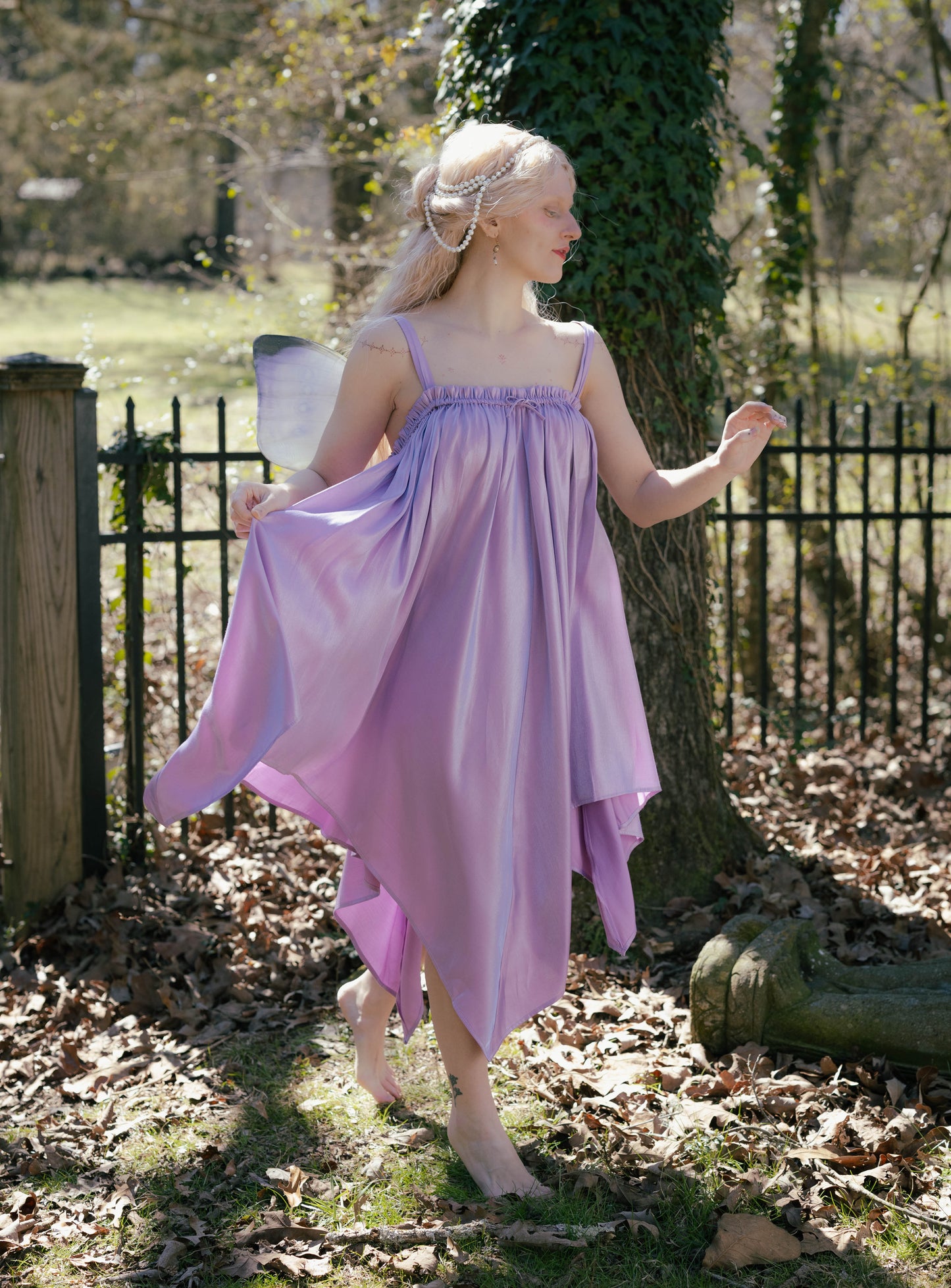 Woman wearing a flowing lavender Flutter Fairy Dress with handkerchief hem standing barefoot outdoors in sunlight