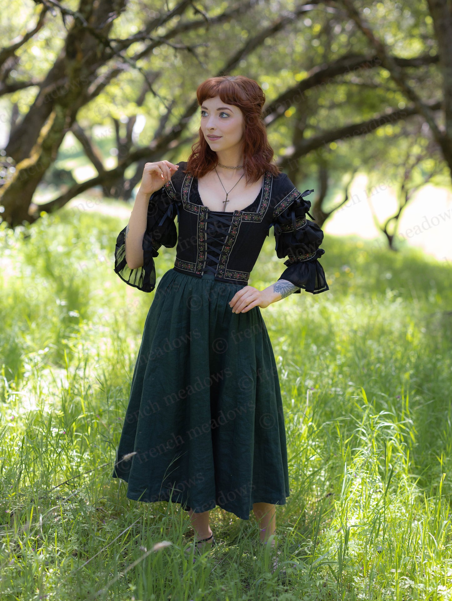 Woman wearing an Evergreen Green Linen Midi Skirt and black corset in a sunlit forest glade.