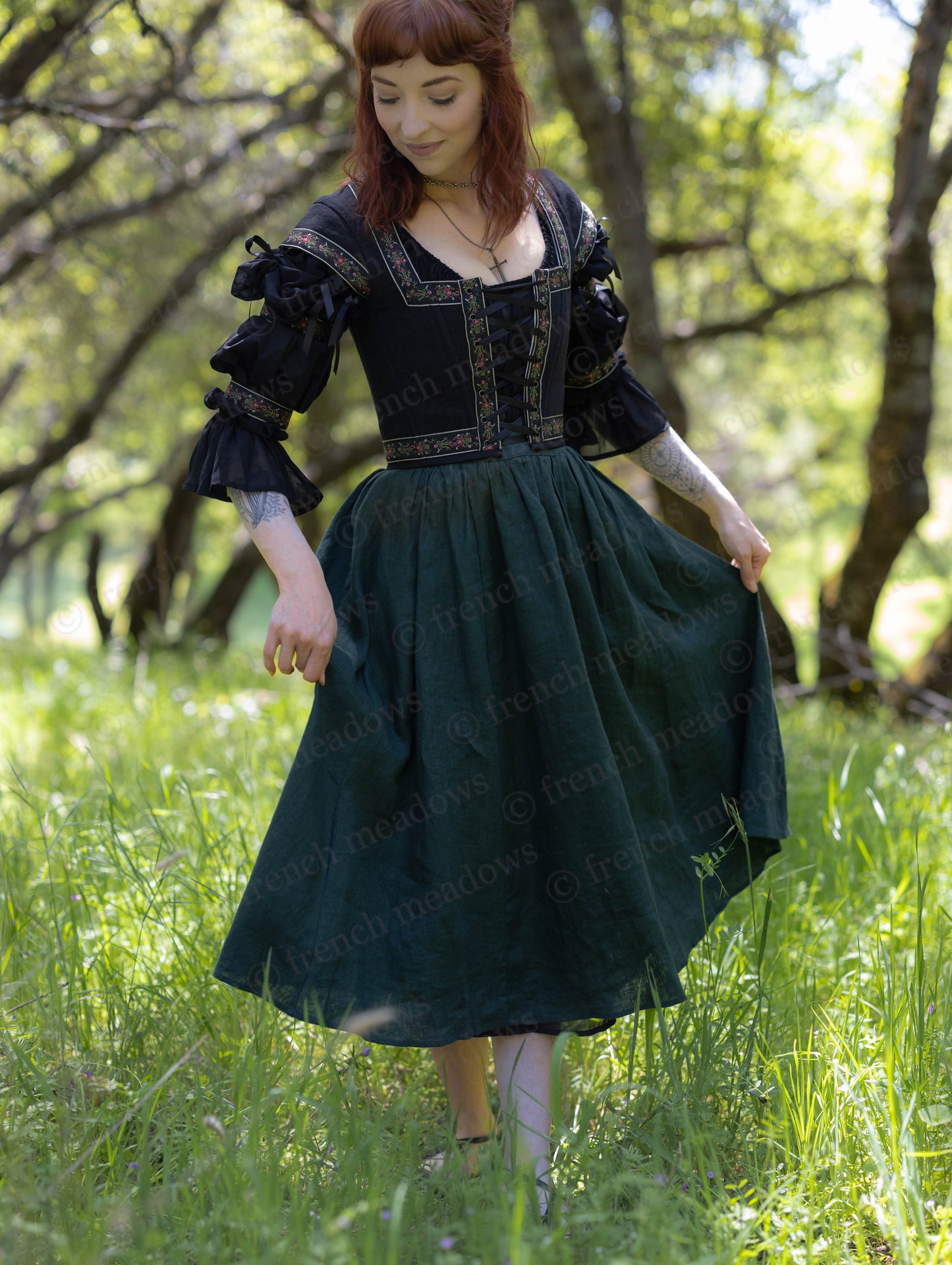 Woman wearing Evergreen Green Linen Midi Skirt with black renaissance-style blouse in a sunlit meadow.