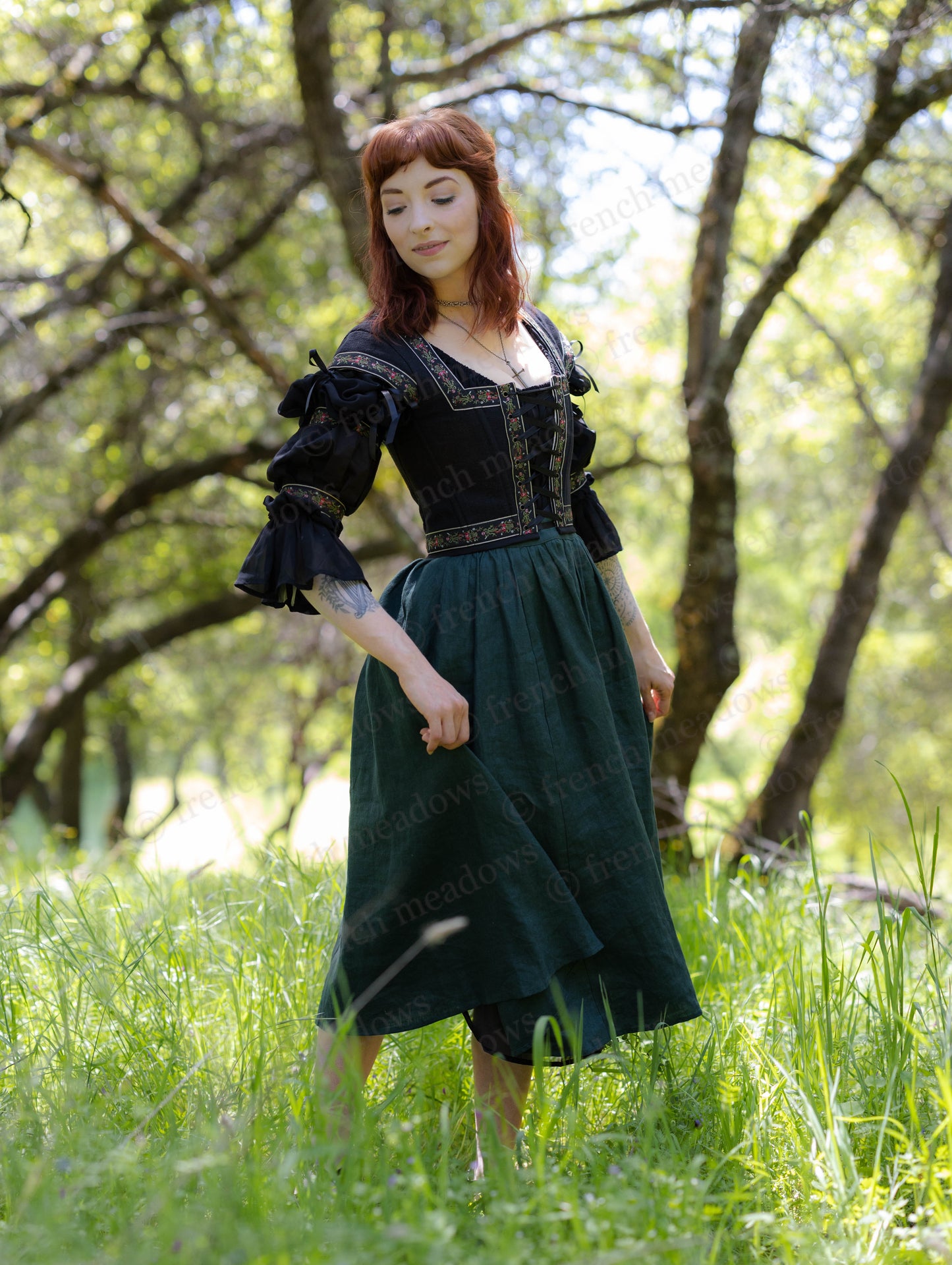 Woman wearing Evergreen Green Linen Midi Skirt in a sunny forest, styled with a black corset and blouse.