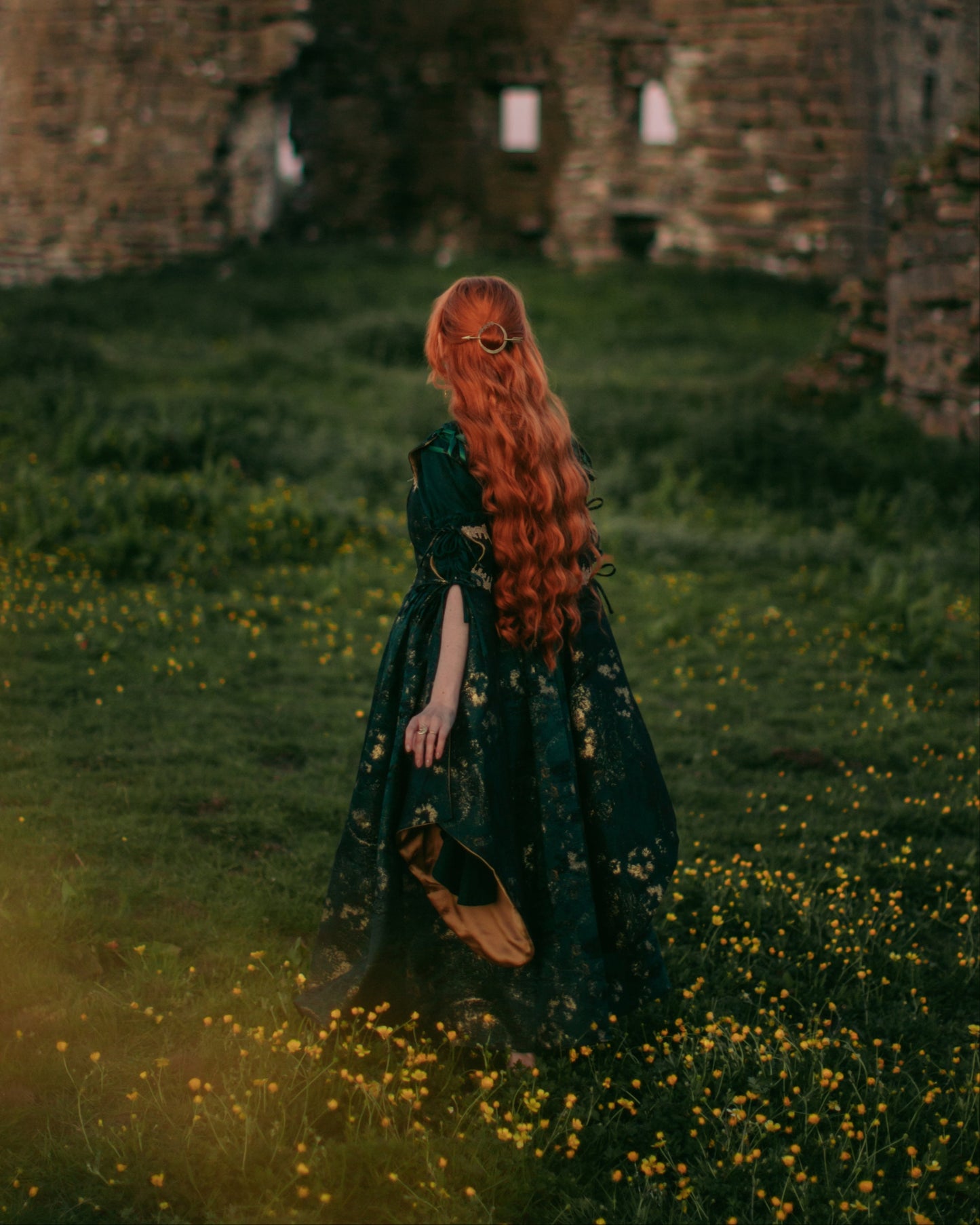 Dark Green Jacquard Corset Dress worn by a red-haired woman standing in a flower-filled field near ruins.
