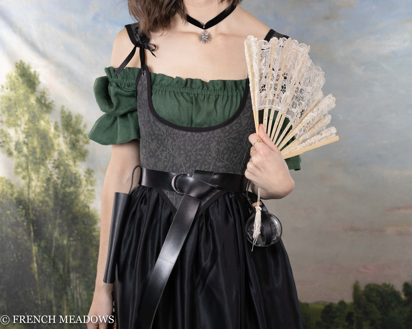 Renaissance Fan Holster in black leather worn with green dress, displaying white lace fan against fantasy backdrop