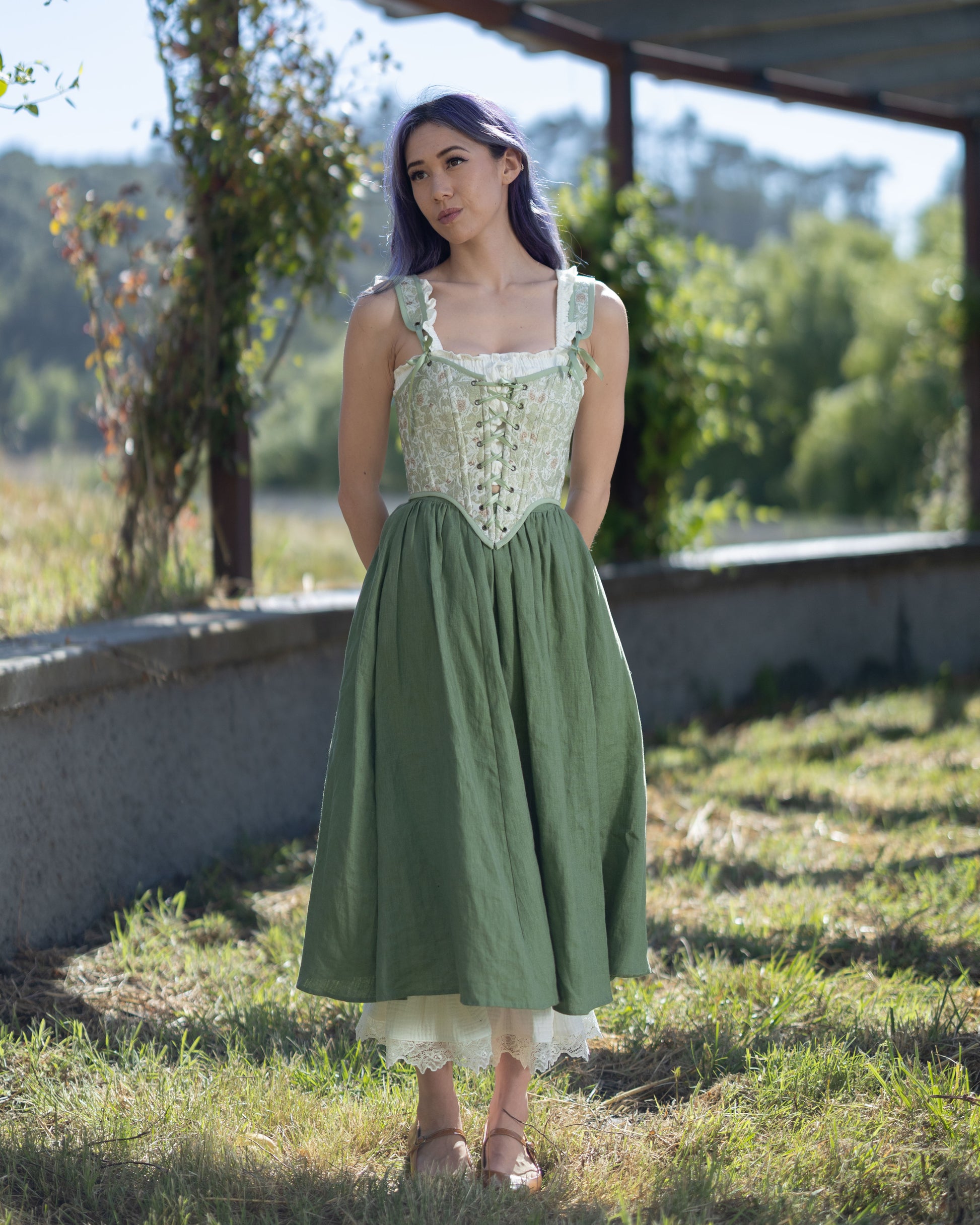 Woman wearing a light green jacquard corset with floral motifs and lace-up front standing outdoors in sunlight
