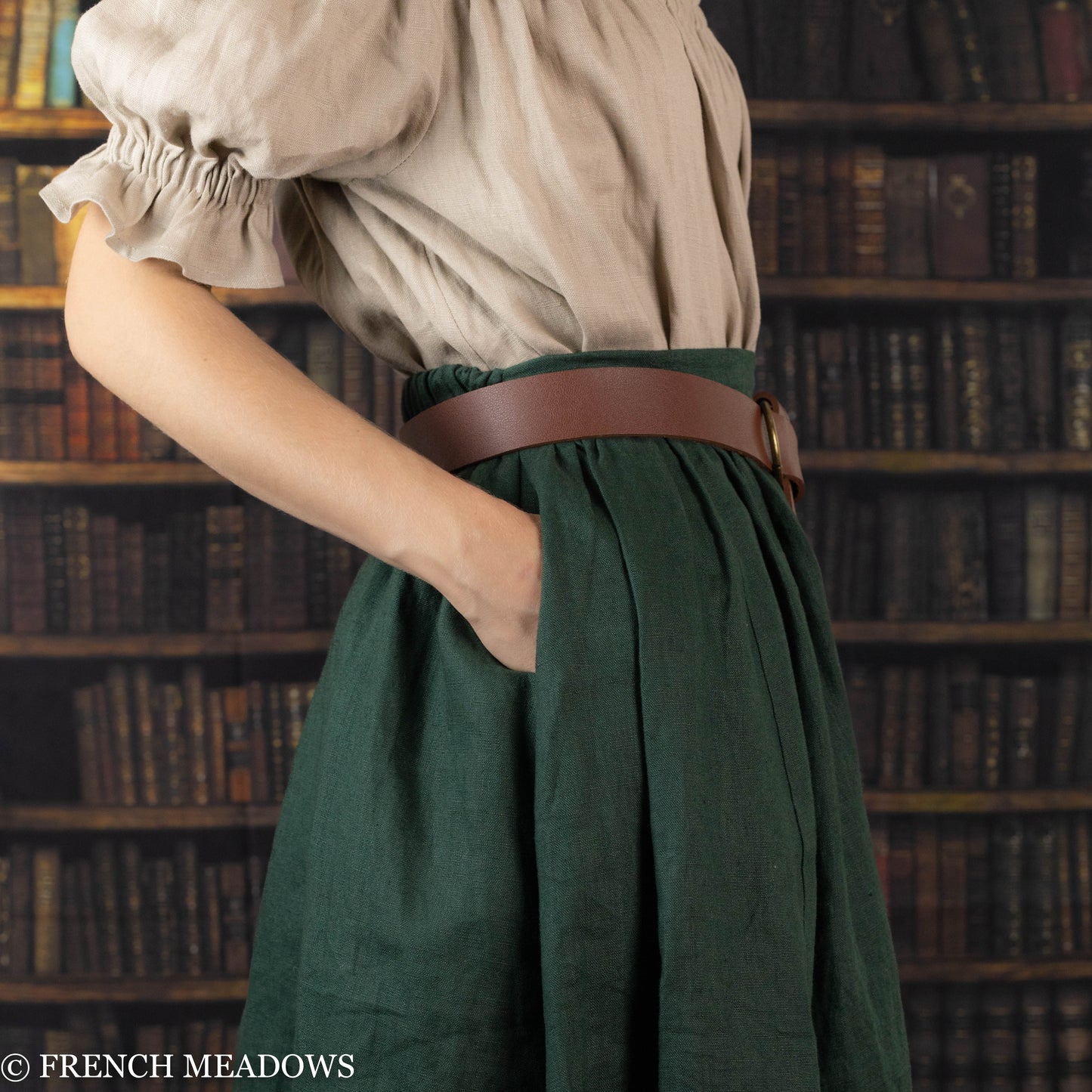 Evergreen Green Linen Midi Skirt with brown leather belt, shown in library setting with hand in hidden pocket