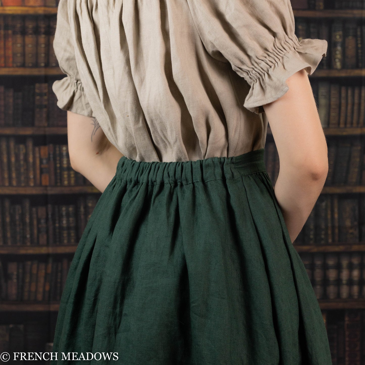 Evergreen Green Linen Midi Skirt shown from back view, featuring gathered waist and flowing silhouette against library backdrop