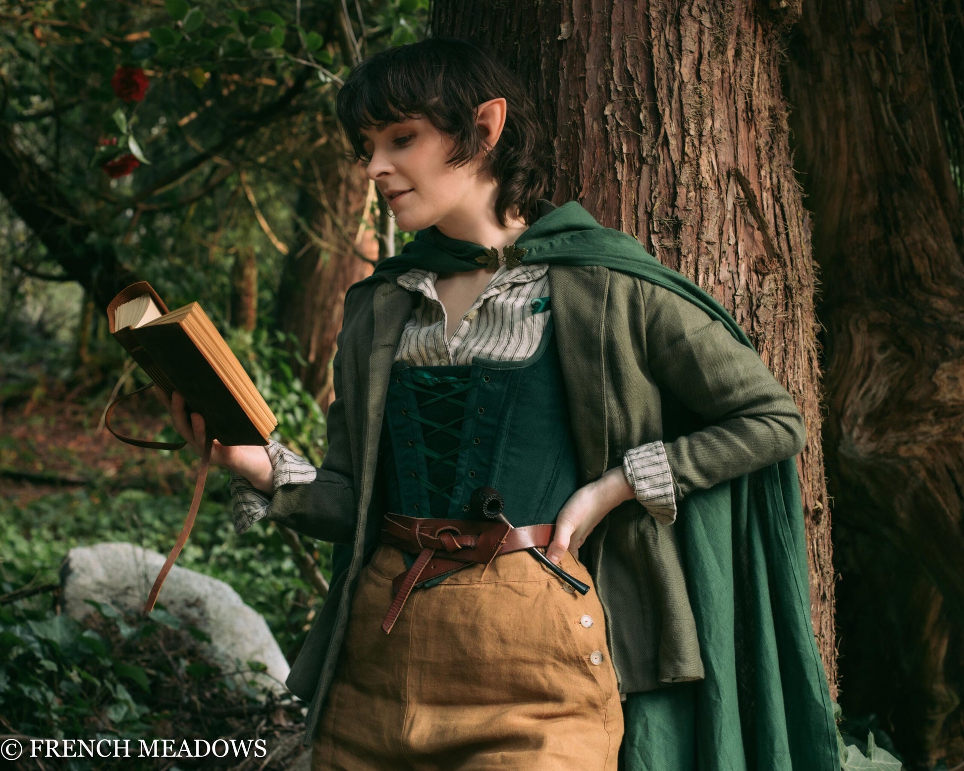 Person wearing Linen Renaissance Cloak in forest setting with medieval-inspired outfit and wooden staff near tree trunk