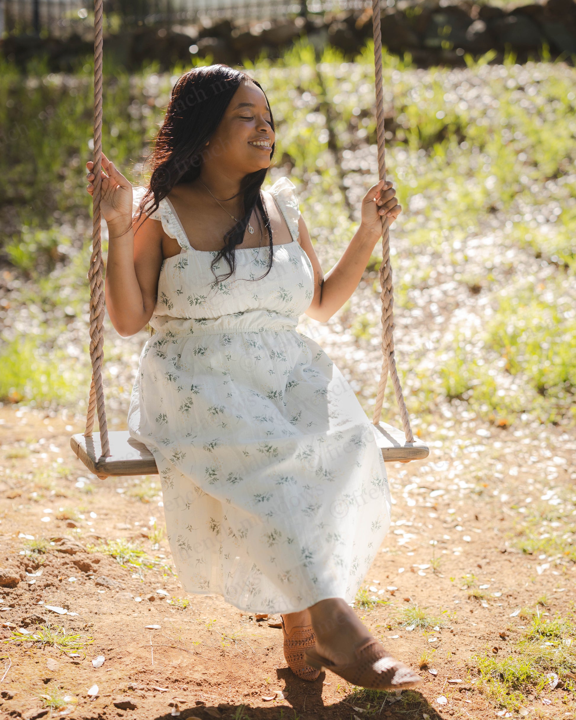 Woman smiling on swing wearing a Floral Milkmaid Dress with ruched bodice and A-line skirt in nature.