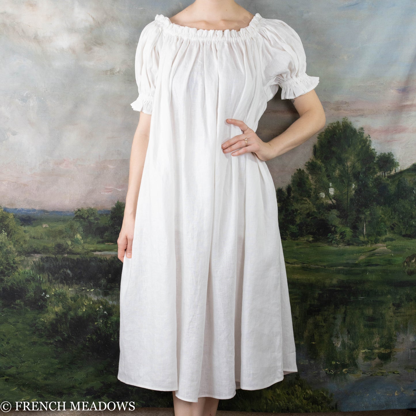 Ivory Short Sleeve Linen Chemise shown off-shoulder with elastic neckline and puff sleeves against pastoral landscape