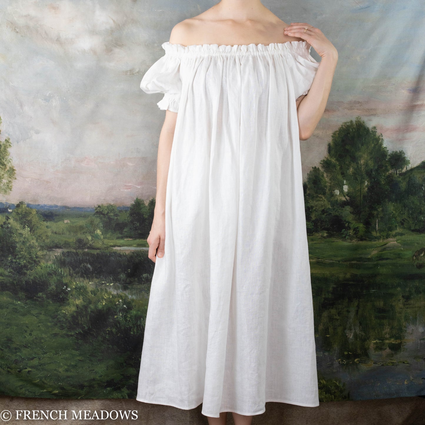 Ivory Short Sleeve Linen Chemise shown as flowy off-shoulder dress with elastic neckline and puff sleeves against pastoral landscape