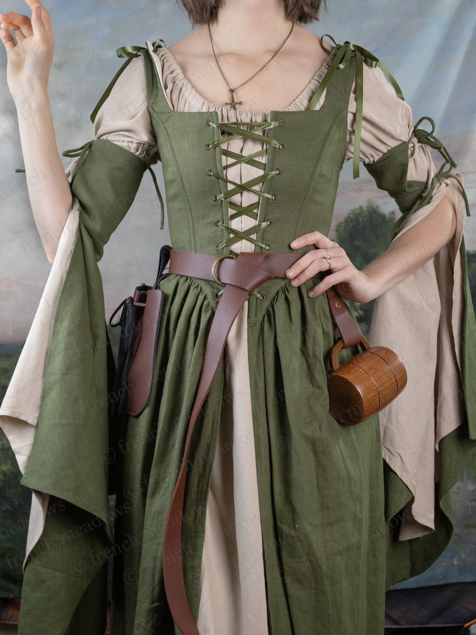 Ivy Green Corset Dress with laced bodice, flowing bell sleeves, and adjustable straps, styled with leather belt and wooden barrel purse