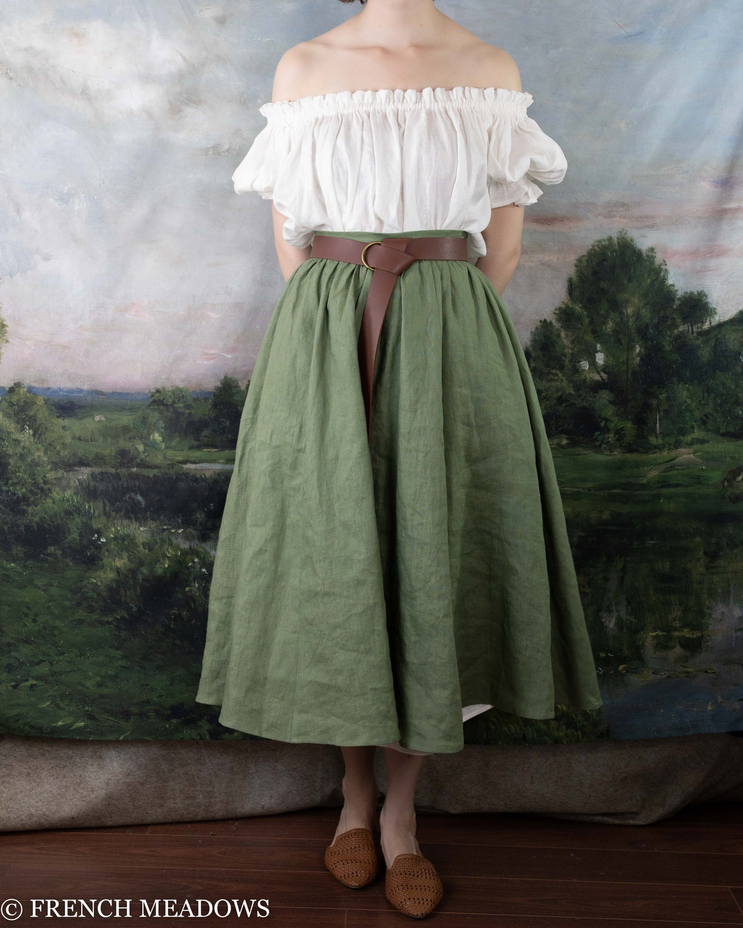 Woman wearing an Ivy Green Linen Midi Skirt paired with a white off-shoulder blouse and brown belt.