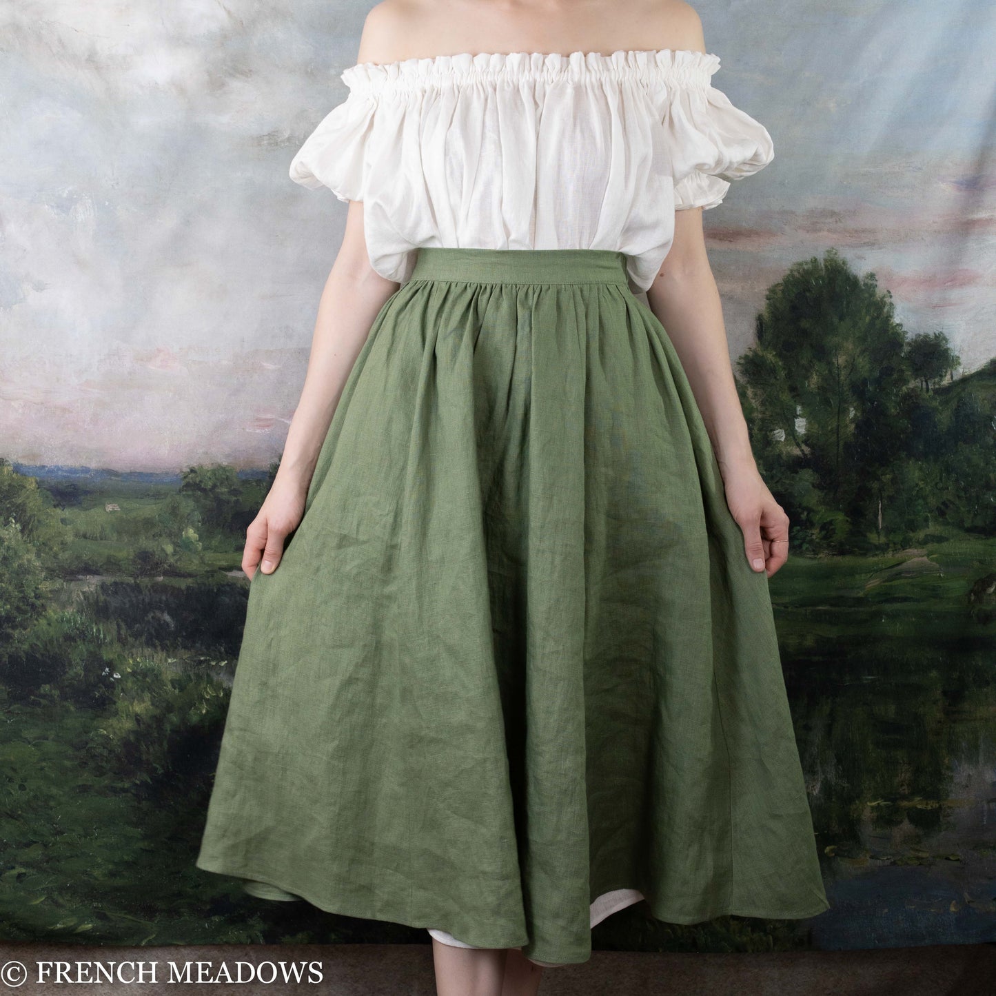 Ivy Green Linen Midi Skirt shown worn with an off-shoulder white blouse against a nature backdrop.