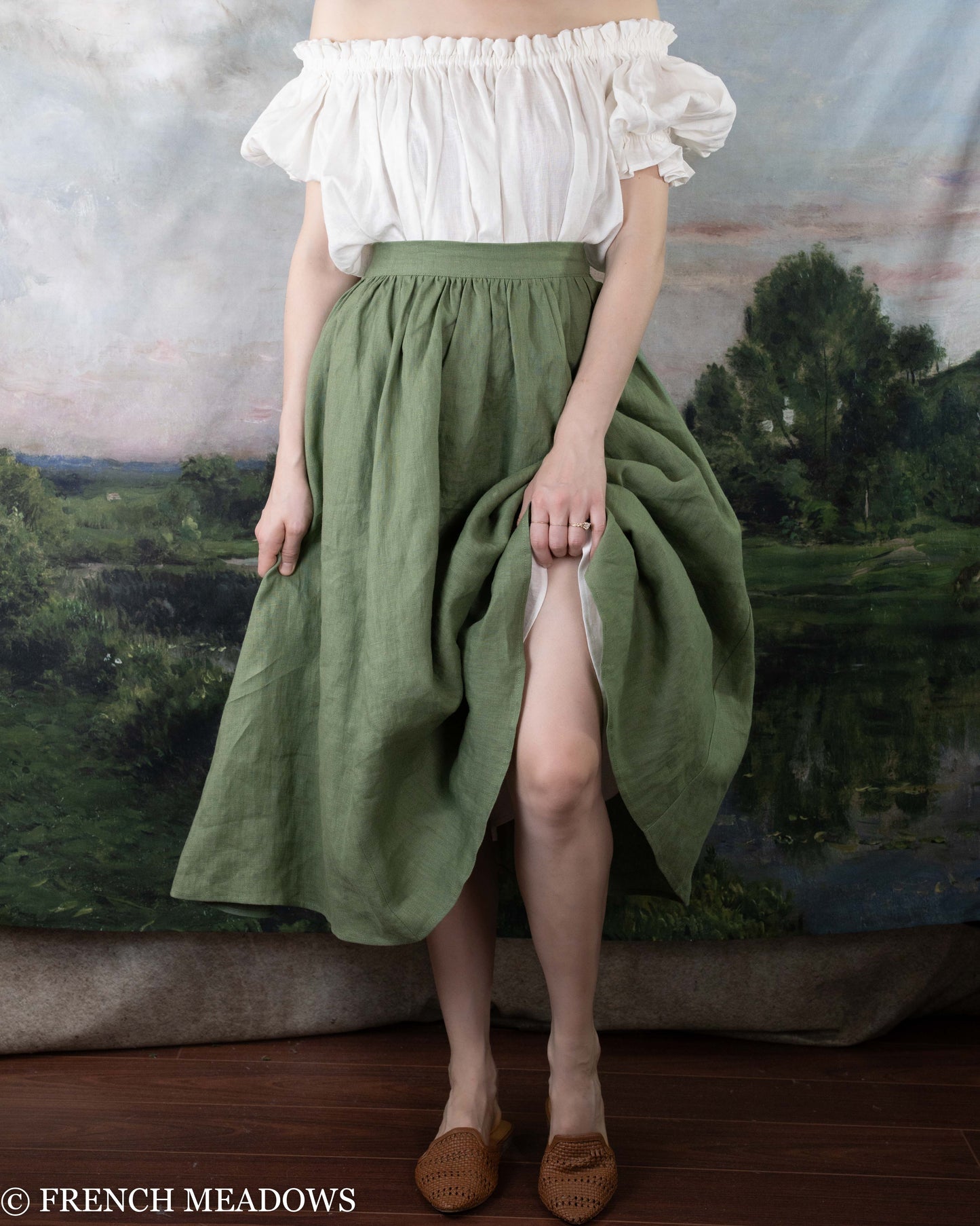 Woman wearing an Ivy Green Linen Midi Skirt with an off-shoulder white top standing indoors.