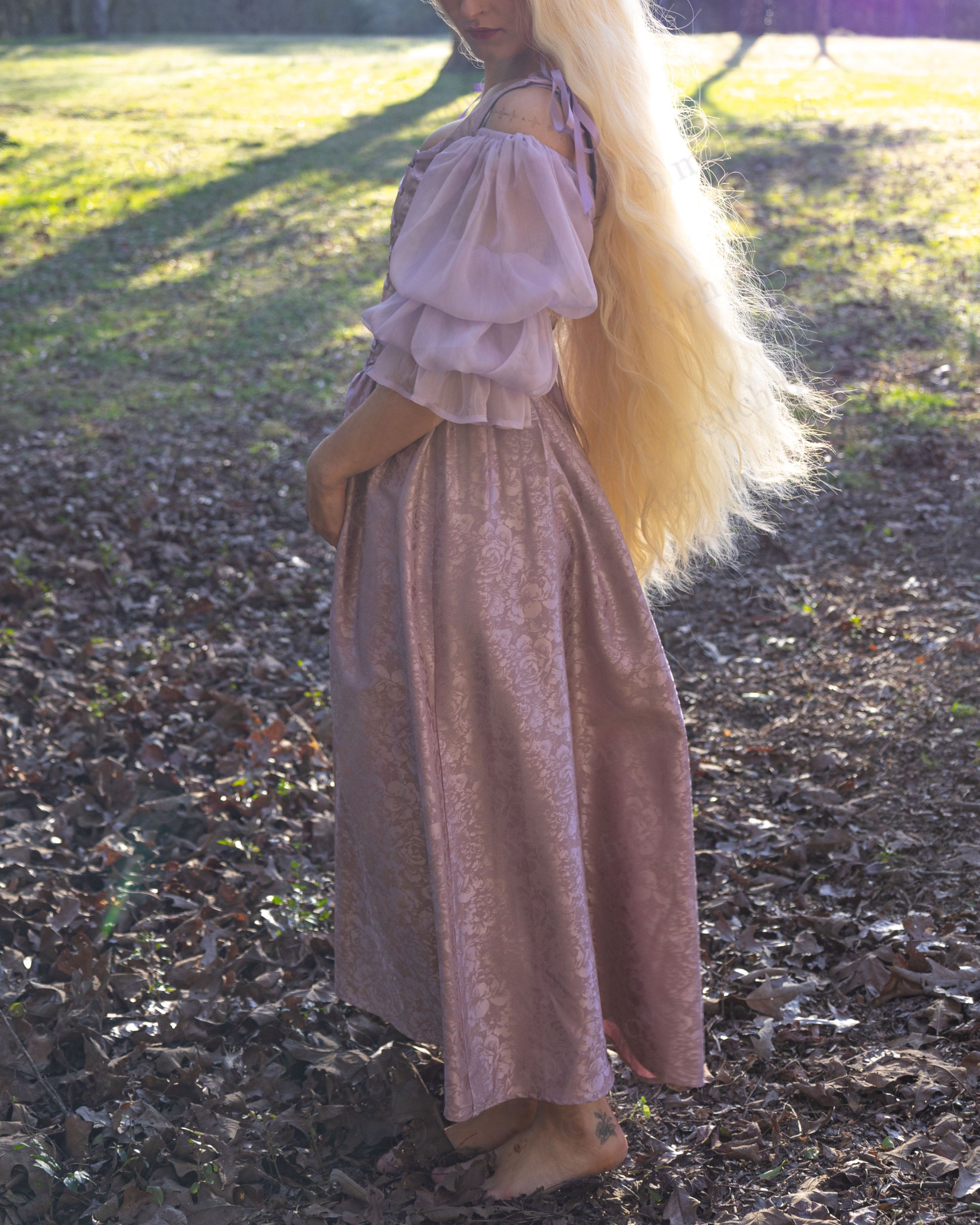 Lavender Floral Satin Corset Dress shown in sunlit woodland setting, displaying flowing sleeves and shimmering jacquard fabric detail