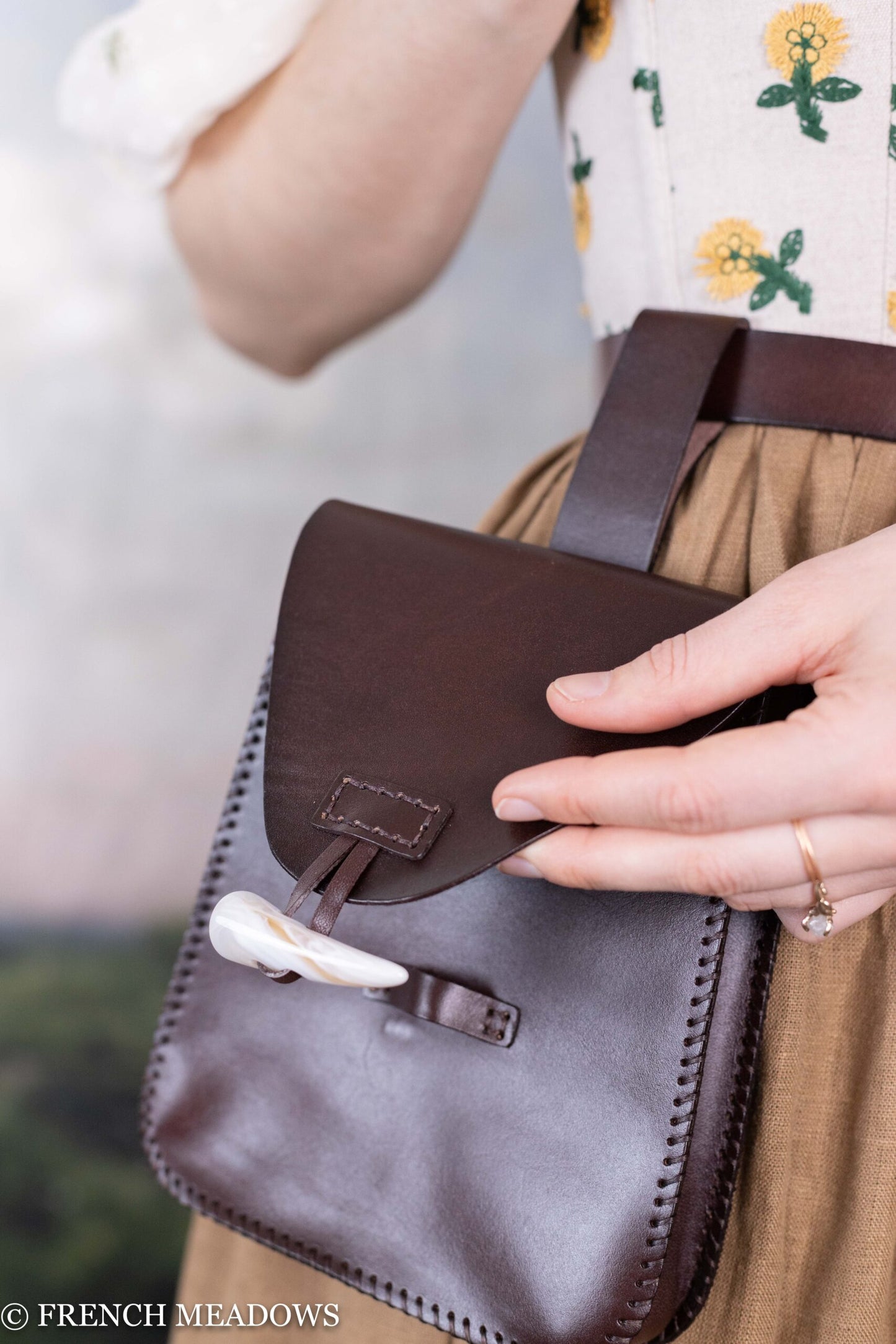 Leather Belt Pouch shown on floral dress wearer, handcrafted dark brown leather with horn toggle closure and decorative stitching