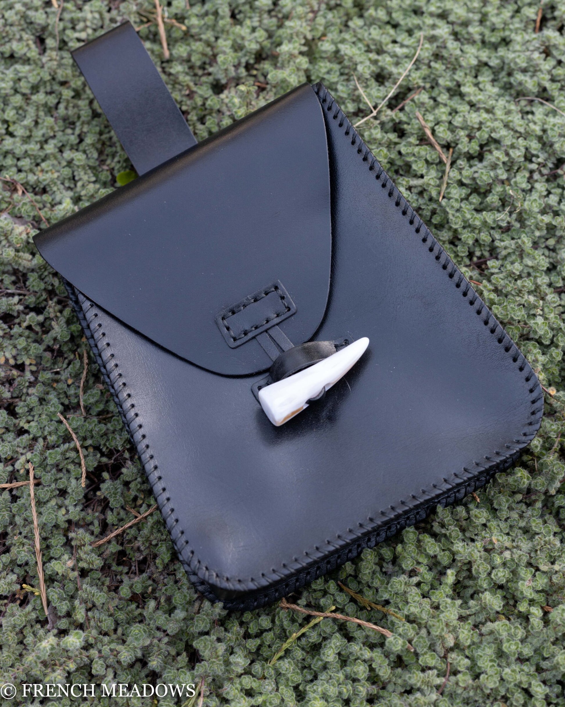 Leather Belt Pouch in black with horn toggle closure, handstitched edges, displayed on mossy ground