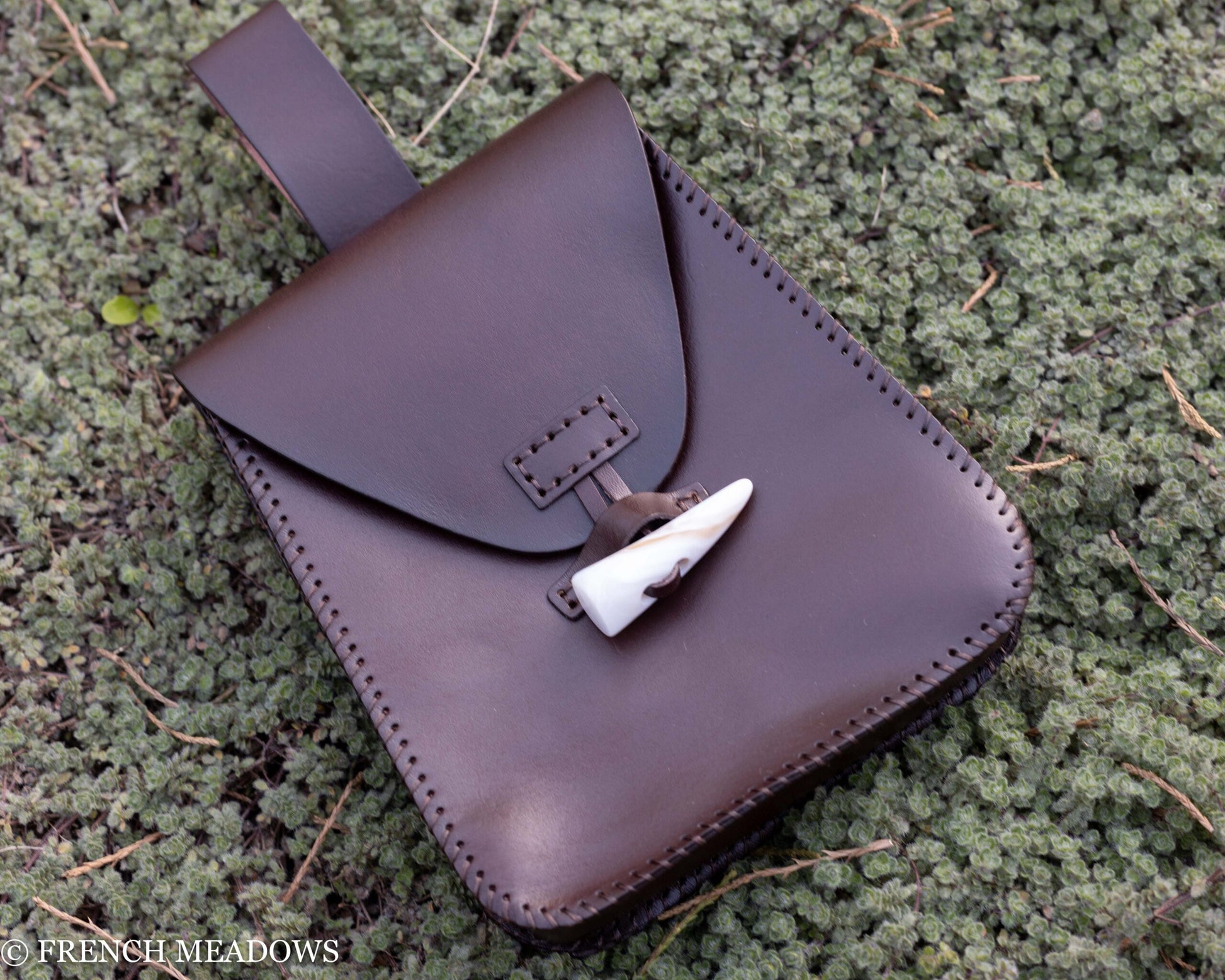 Brown leather belt pouch with buffalo horn toggle closure shown on mossy ground, handcrafted medieval style accessory