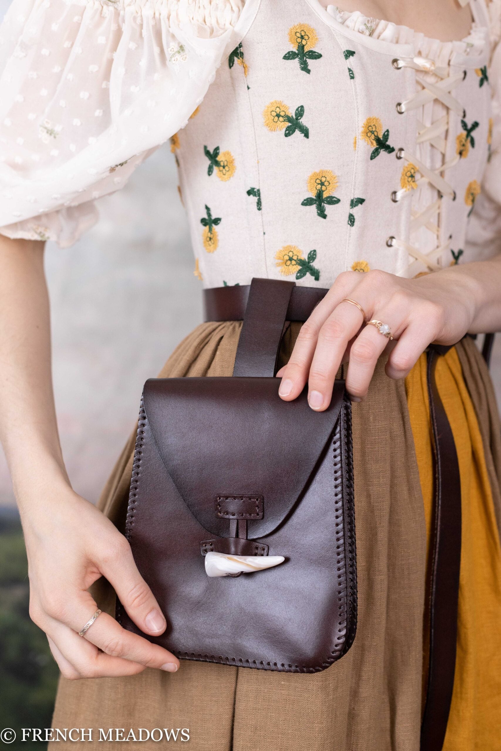 Leather Belt Pouch shown on model wearing floral dress, displaying dark brown leather construction with horn toggle closure