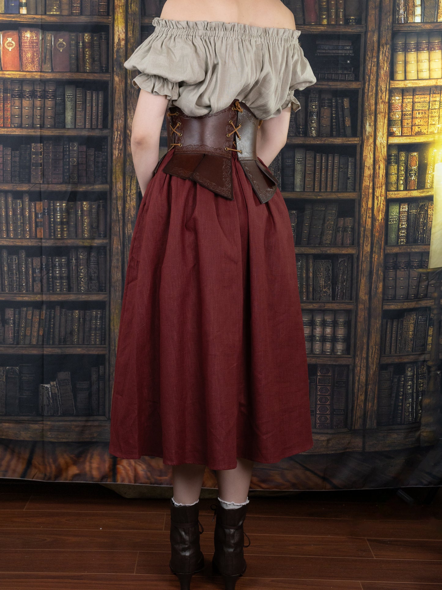 Debossed Leather Underbust Corset shown with burgundy skirt and grey top against vintage library backdrop, medieval-style stamped design
