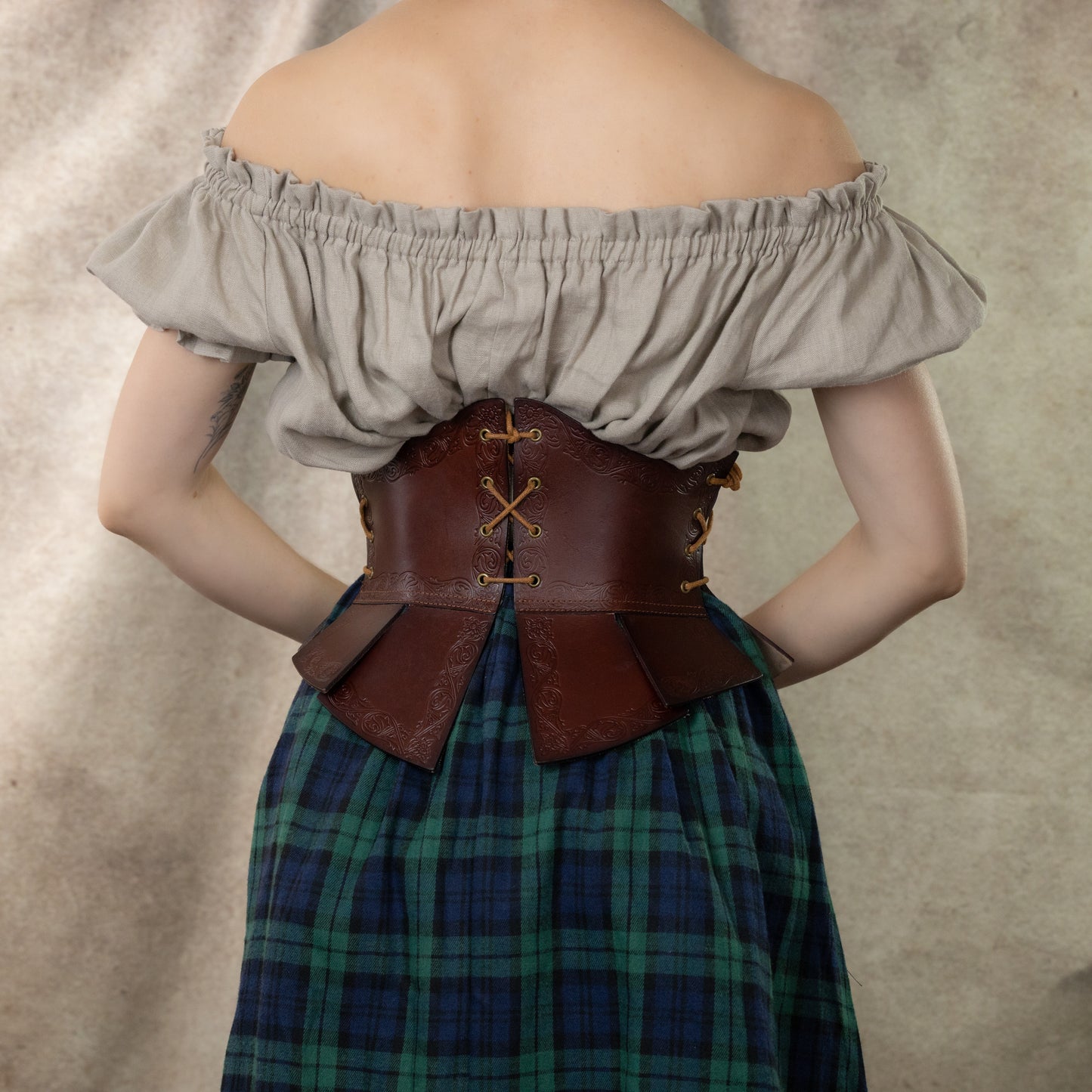 Debossed leather underbust corset with medieval pattern shown on plaid dress, displaying intricate back lacing and waist tabs