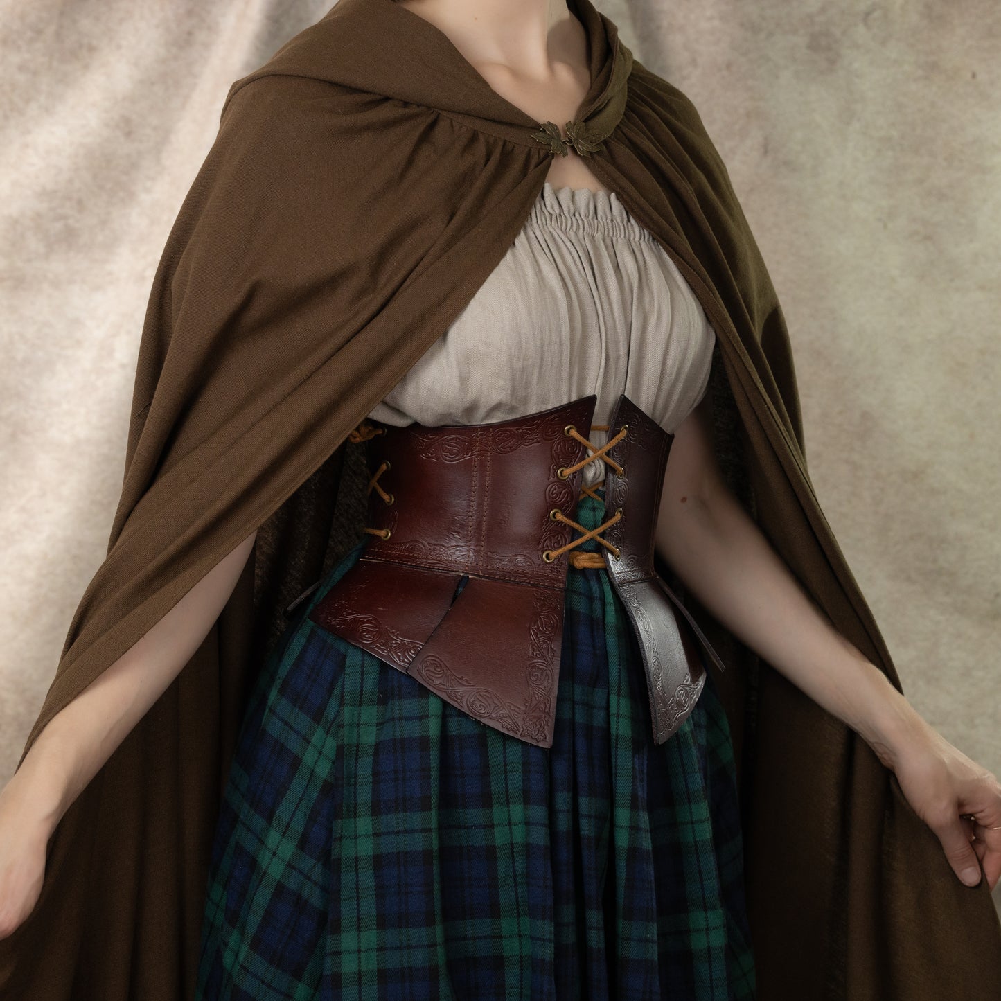Debossed leather underbust corset worn with plaid skirt and brown cloak, showcasing medieval stamped pattern and waist tabs