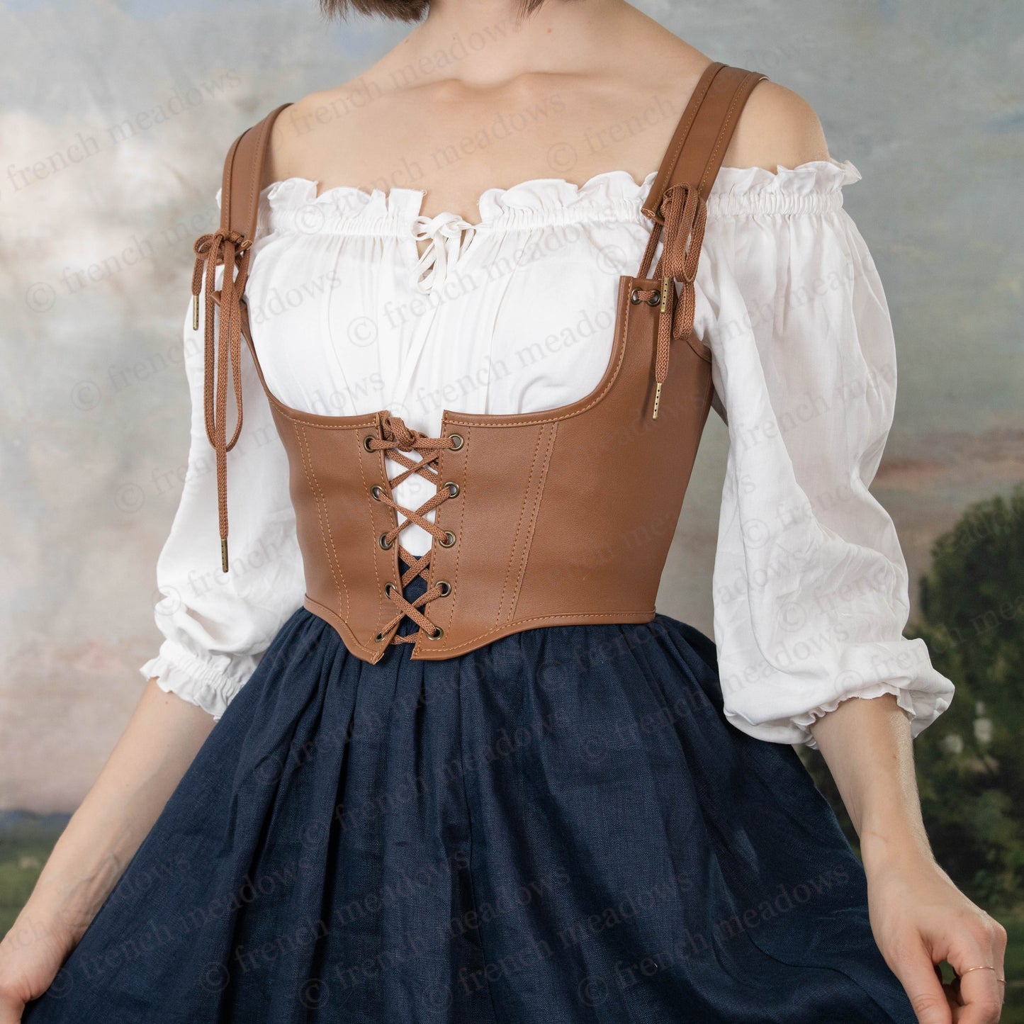 Leather underbust corset belt worn over white peasant blouse and navy skirt, laced up with adjustable shoulder straps