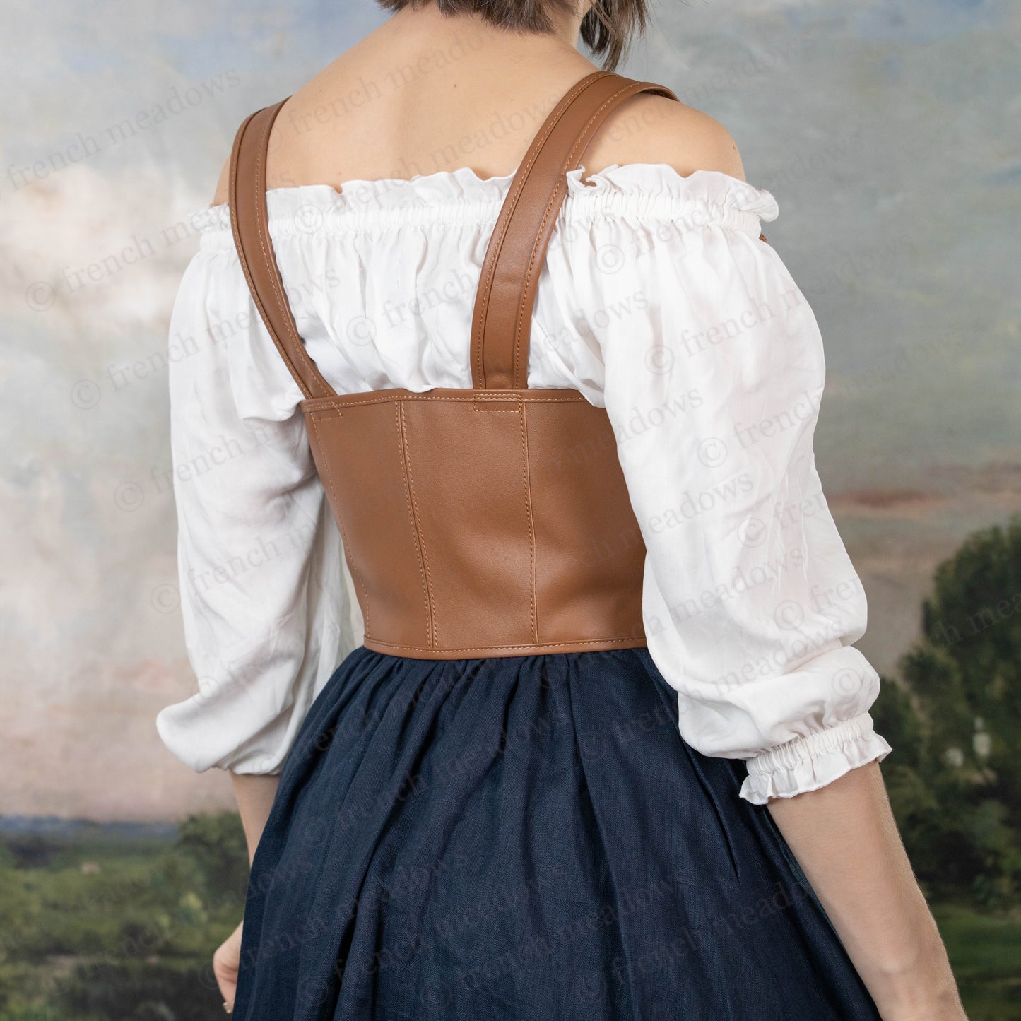 Brown leather underbust corset belt worn over white peasant blouse with navy skirt, shown from back view