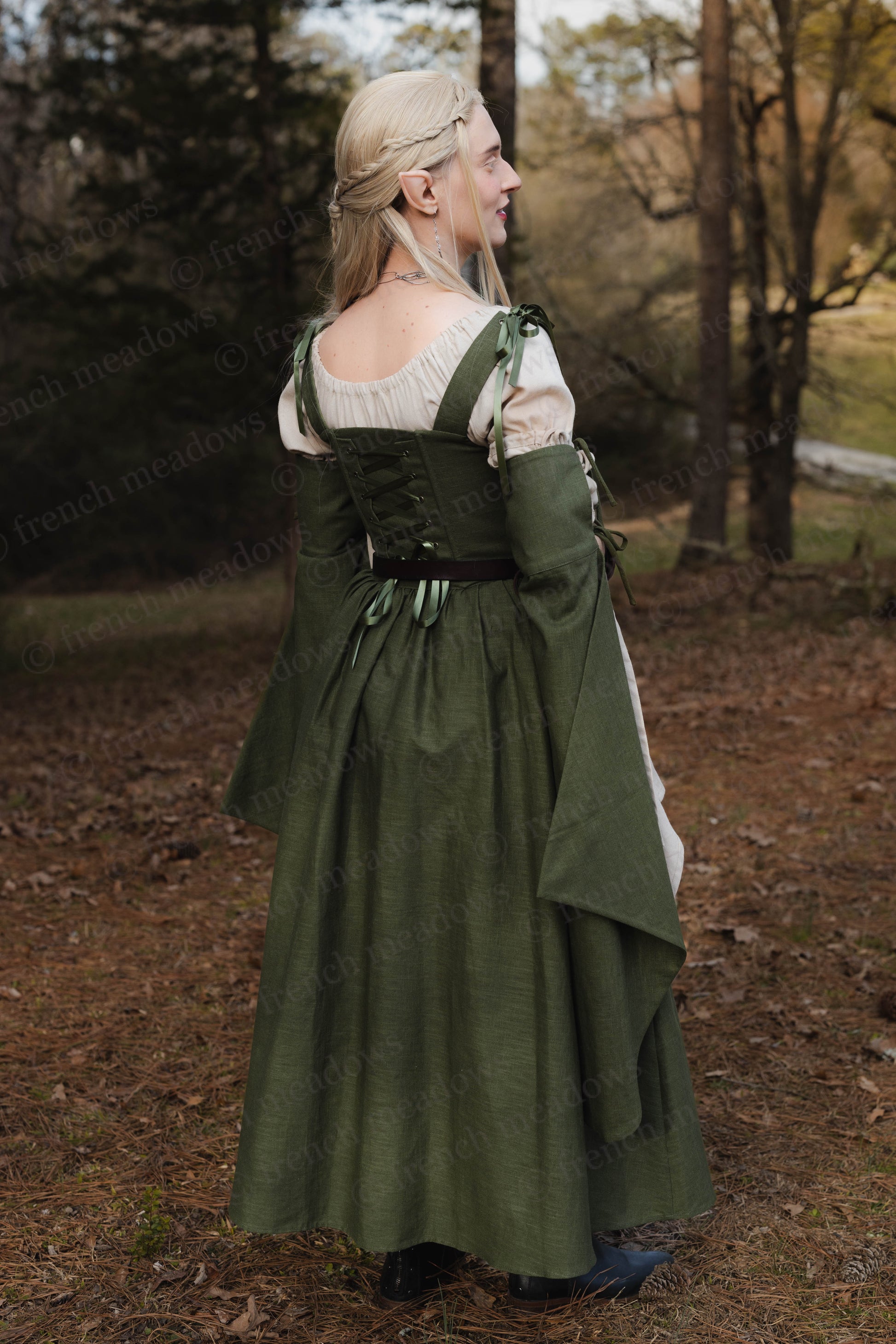 Ivy Green Corset Dress shown from back view in forest setting, featuring laced bodice, flowing skirt and bell sleeves in natural light