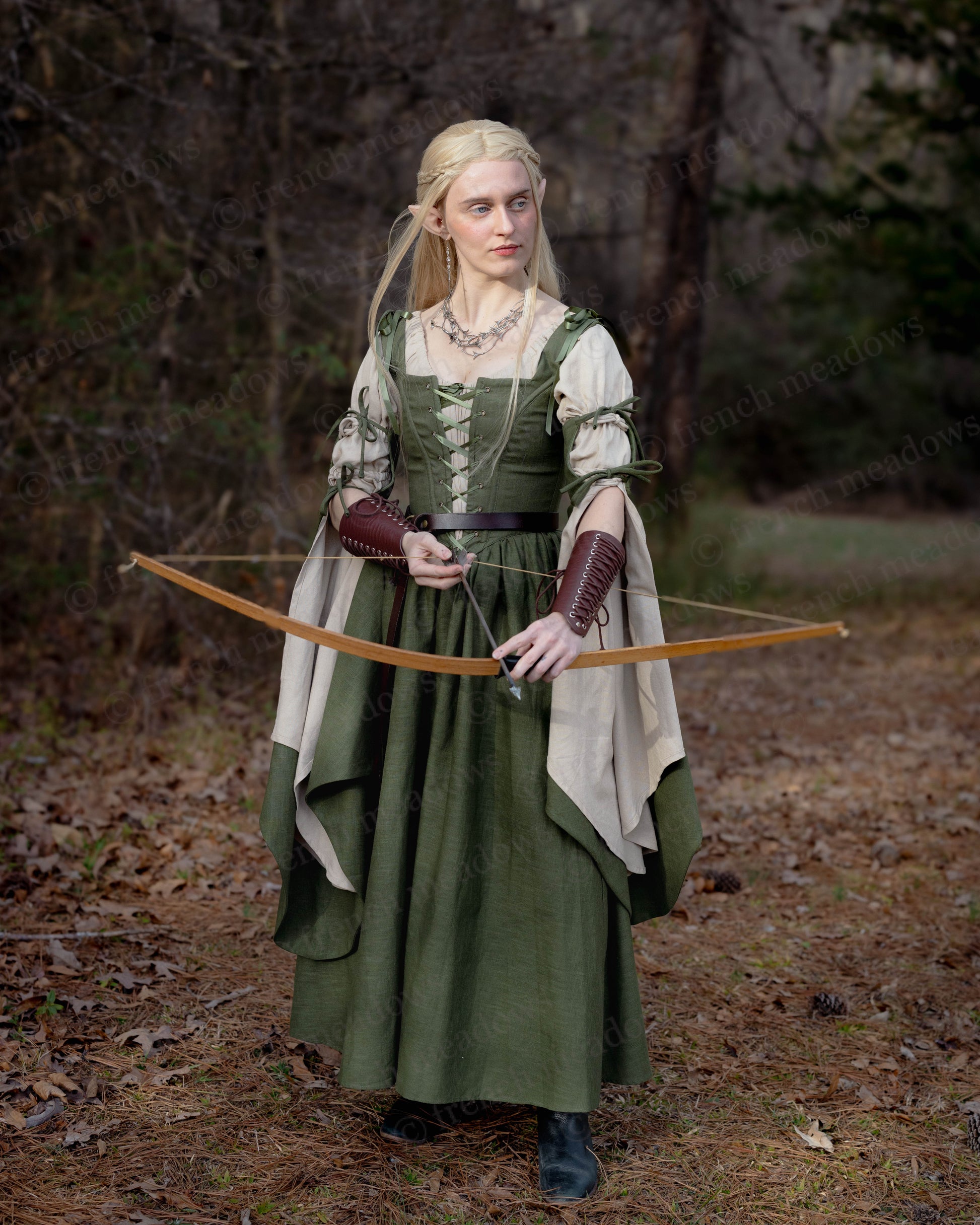 Ivy Green Corset Dress with bell sleeves shown in forest setting, paired with leather bracers and wooden bow