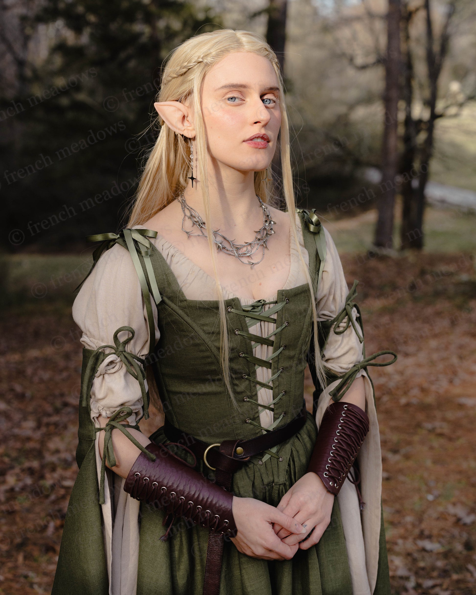 Ivy Green Corset Dress shown in woodland setting with medieval-style lacing, bell sleeves, and leather accessories on model
