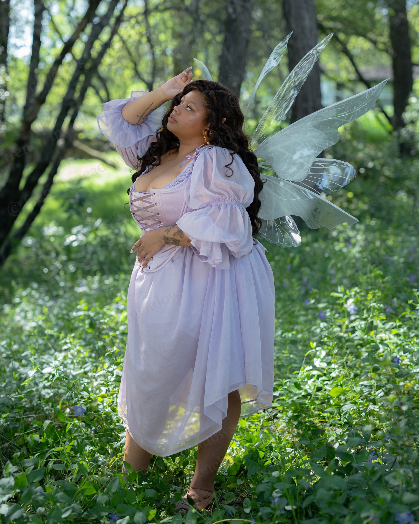 Woman wearing Lilac Satin 18th Century Stays with fairy wings in a sunlit forest surrounded by greenery and flowers.