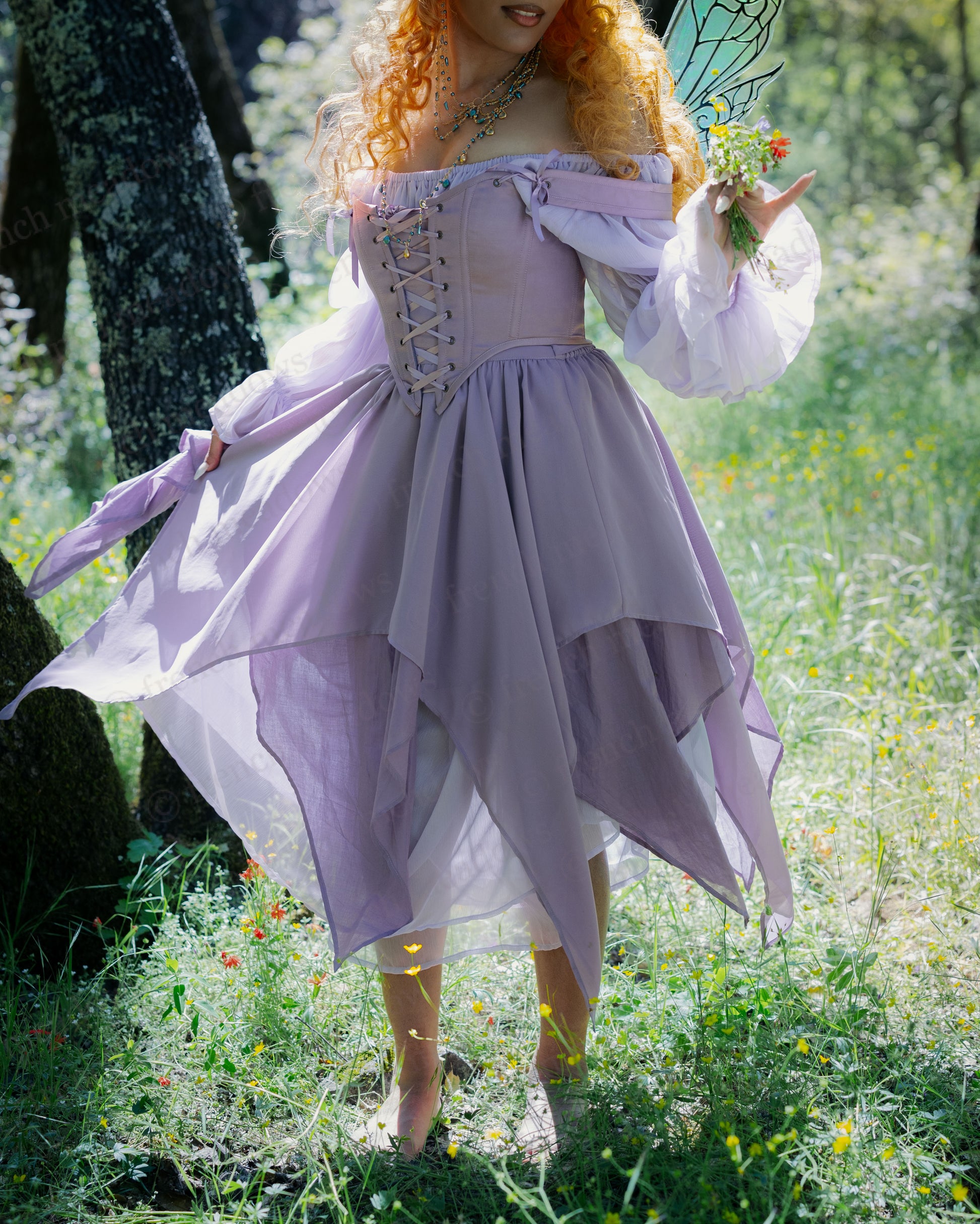 Woman wearing a lavender layered Flower Fairy Skirt with pointed hem, standing barefoot in a sunlit forest clearing.