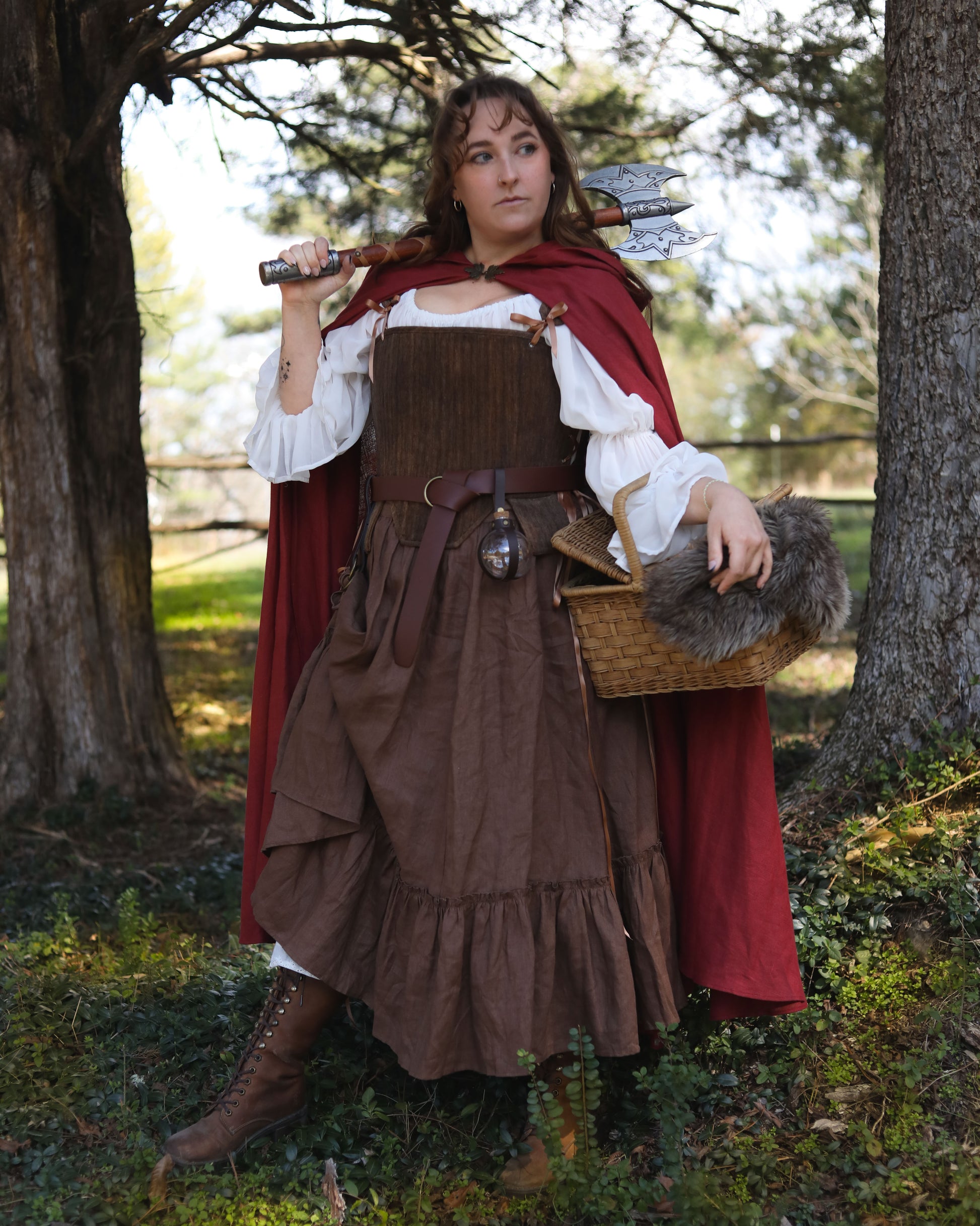 Woman wearing a red linen renaissance cloak over rustic brown and white medieval-style clothing holding a basket with fur lining