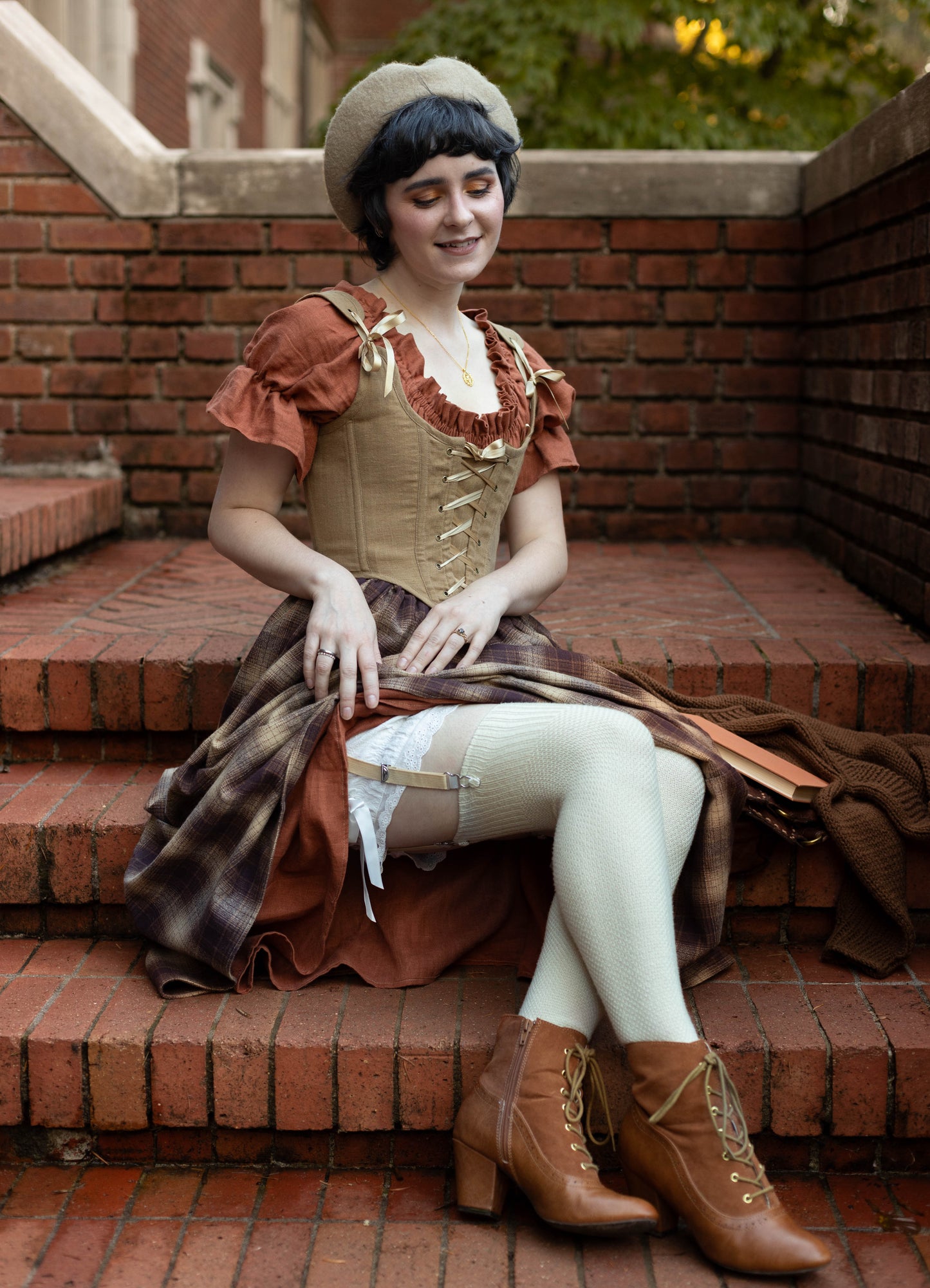 Person wearing Victorian Bloomers in vintage-inspired outfit with corset and plaid skirt, sitting on brick steps outdoors