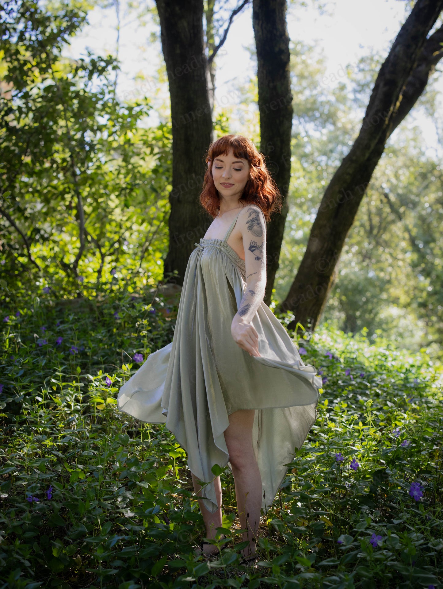Woman wearing flowing green Flutter Fairy Dress with handkerchief hem in sunlit forest setting