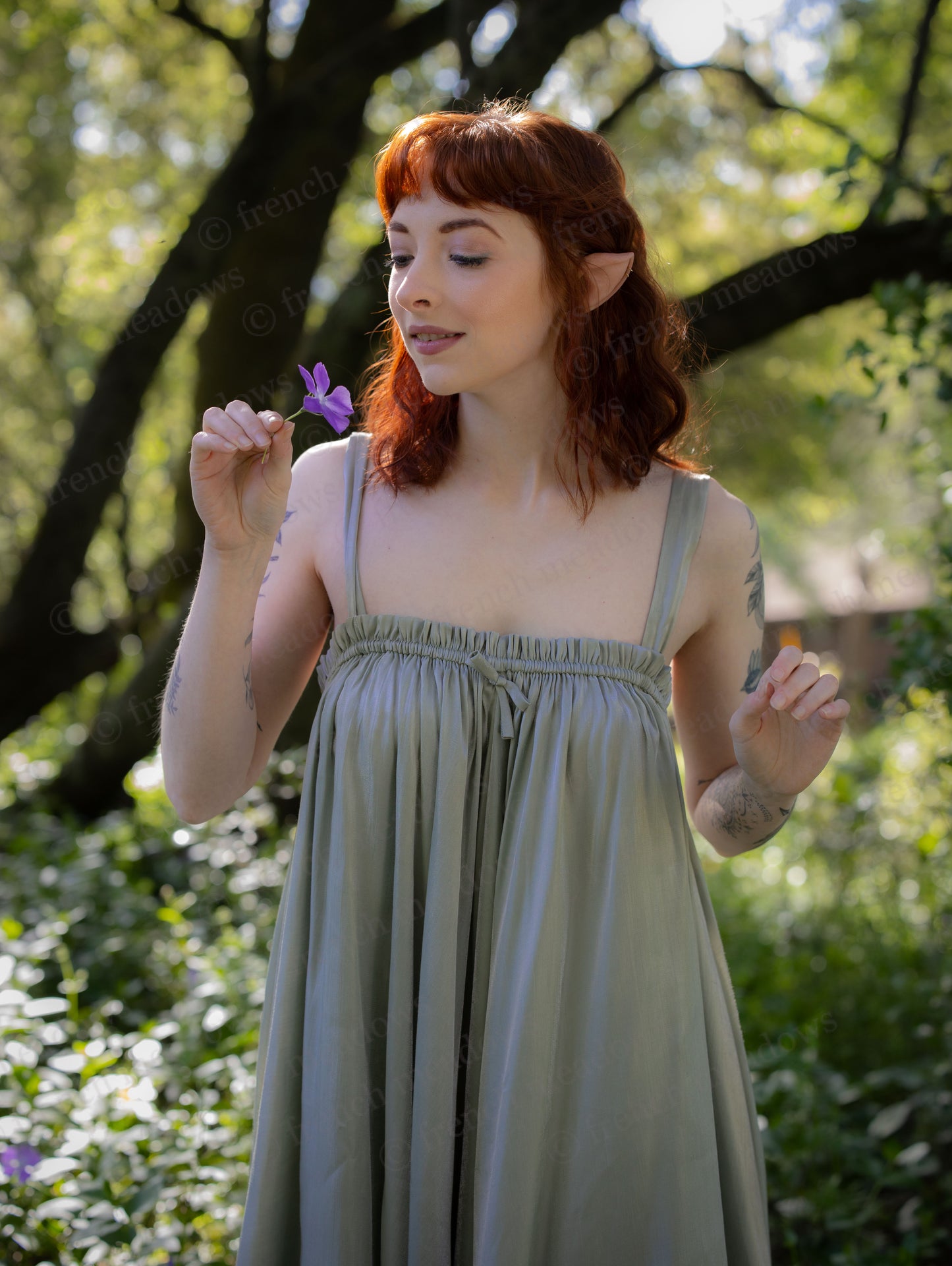 Woman in a garden wearing a green Flutter Fairy Dress with adjustable straps and a flowing handkerchief hem.