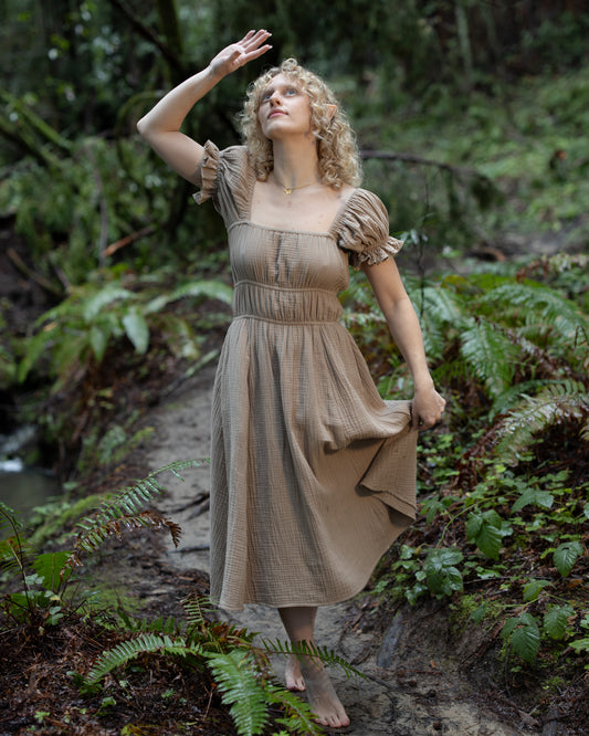 Woman wearing a Brown Milkmaid Dress standing barefoot in a lush forest setting with greenery around her.